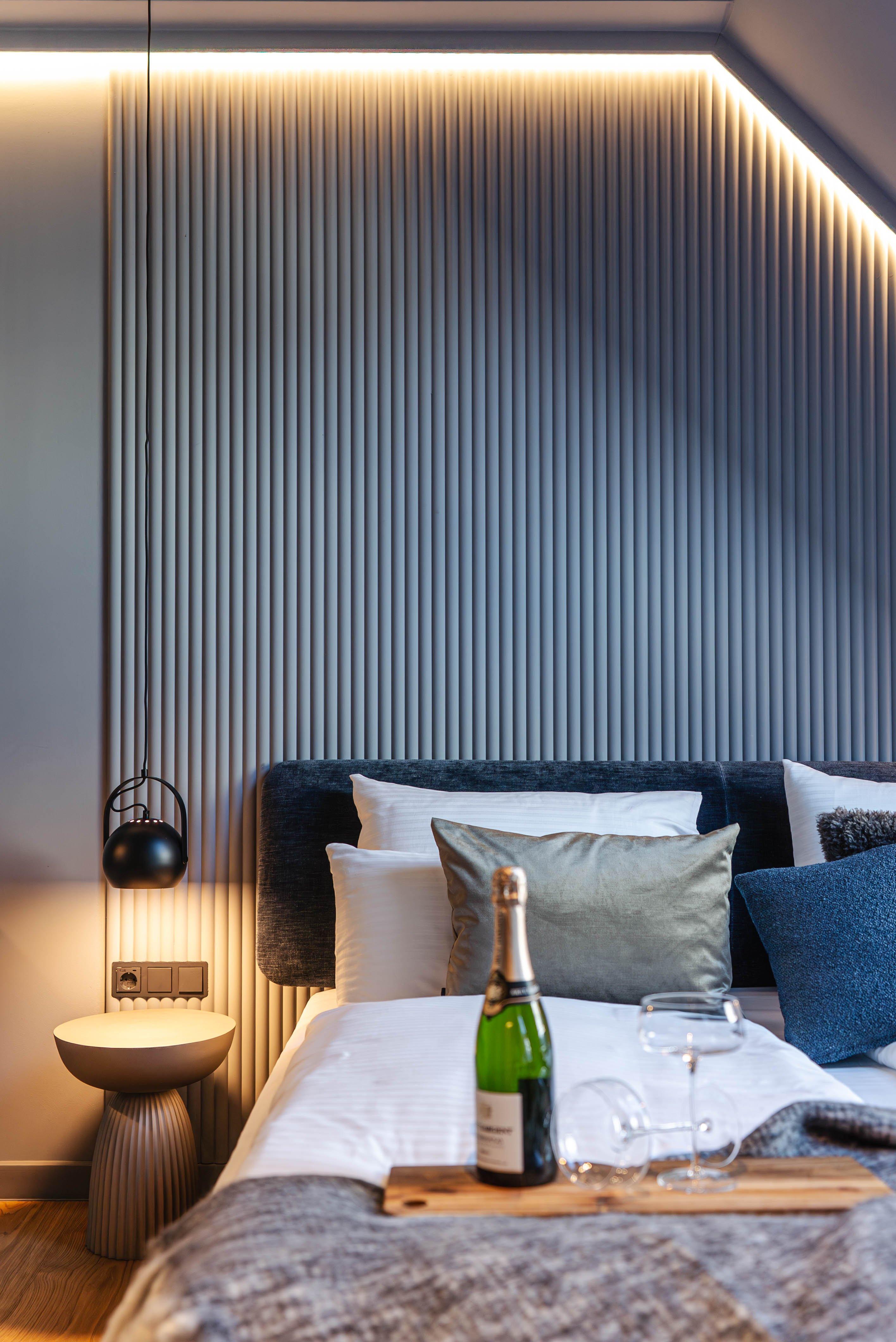 Lit avec coussins, lampe suspendue, bouteille de champagne et verres sur plateau en bois.