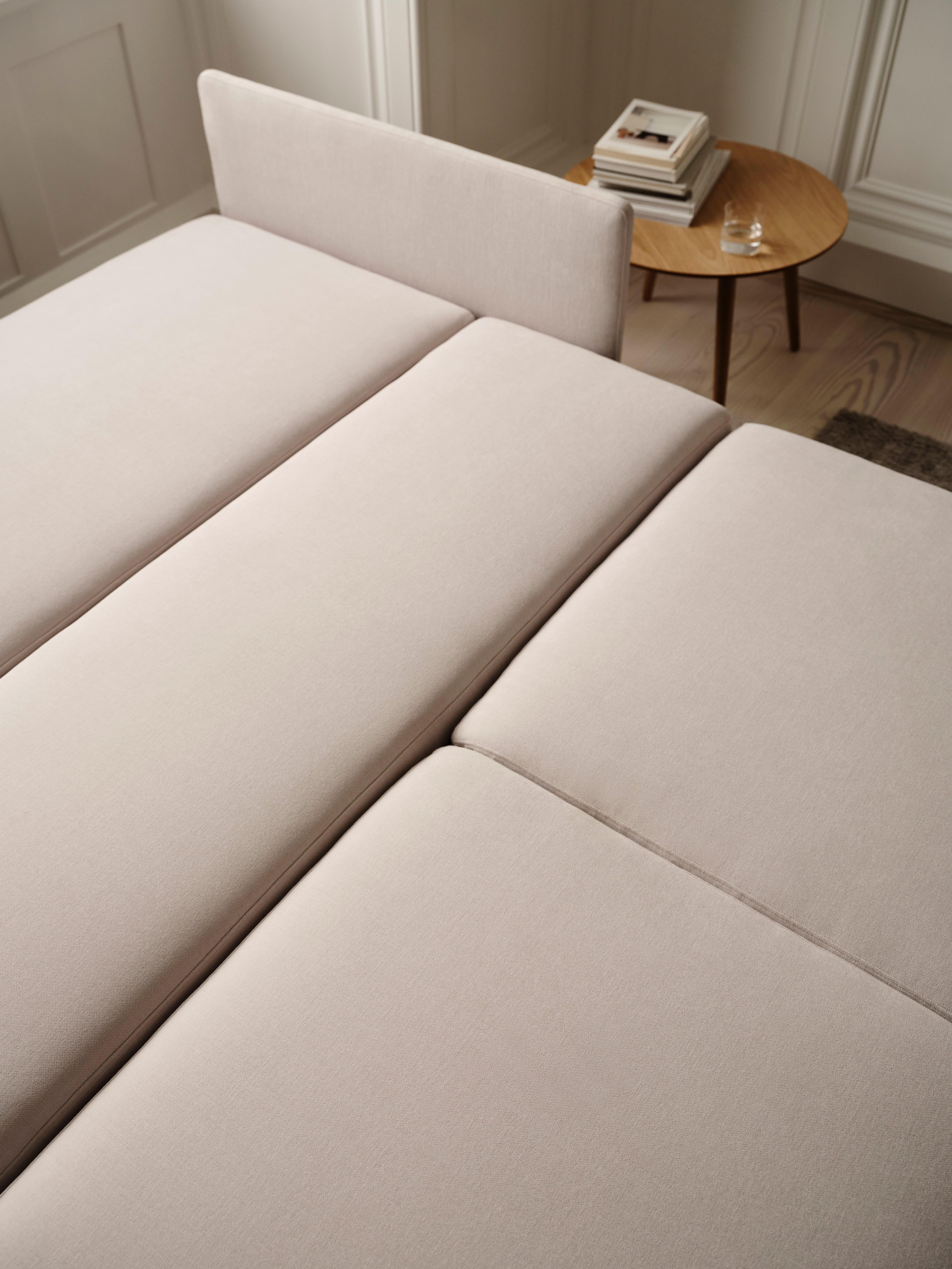 Beige upholstered daybed with a small wooden side table holding books and a glass.