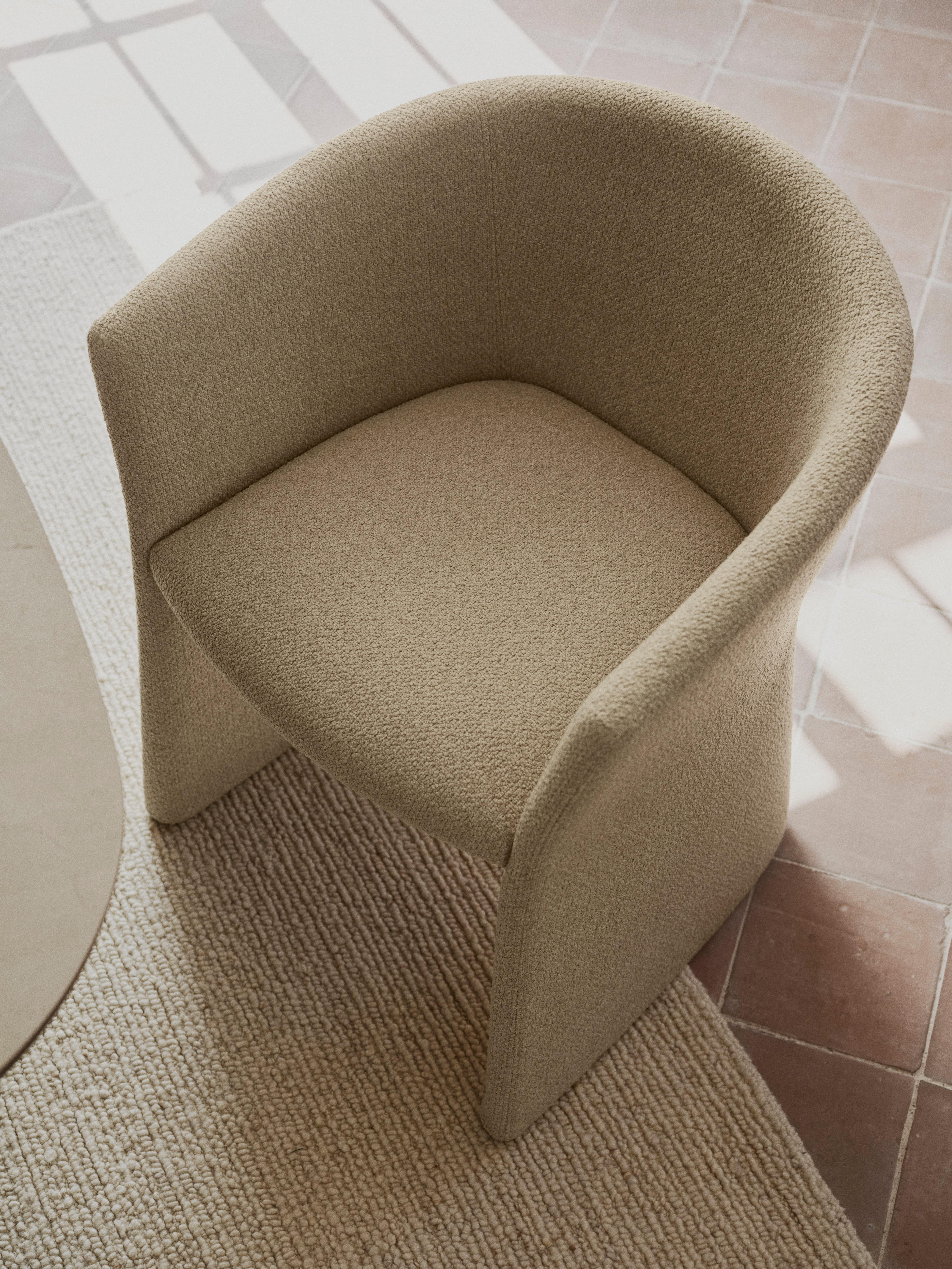 Bouclé upholstered tub chair with curved back and seat cushion.