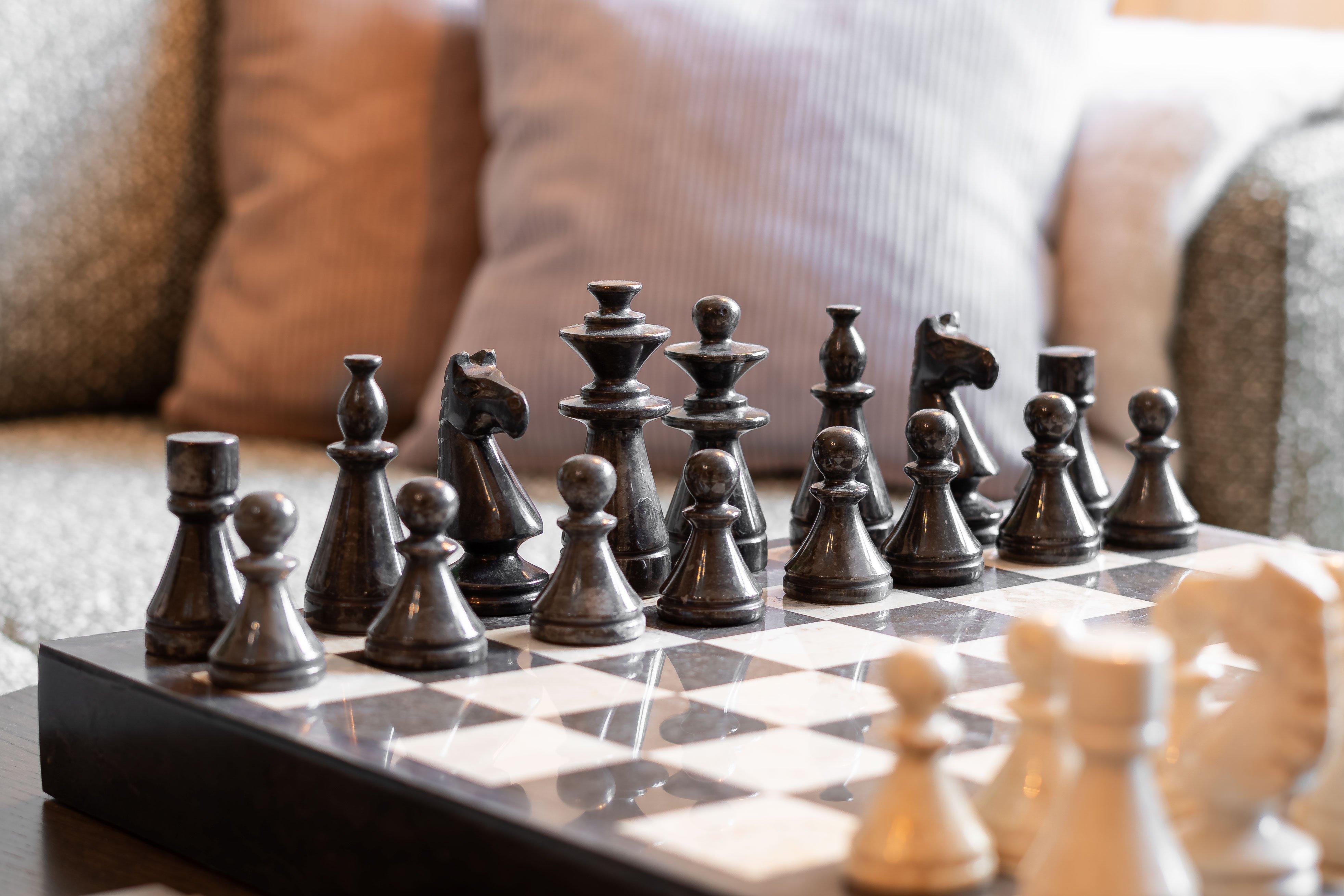 Pièces d'échecs noires sur un échiquier, fond de coussins flous.