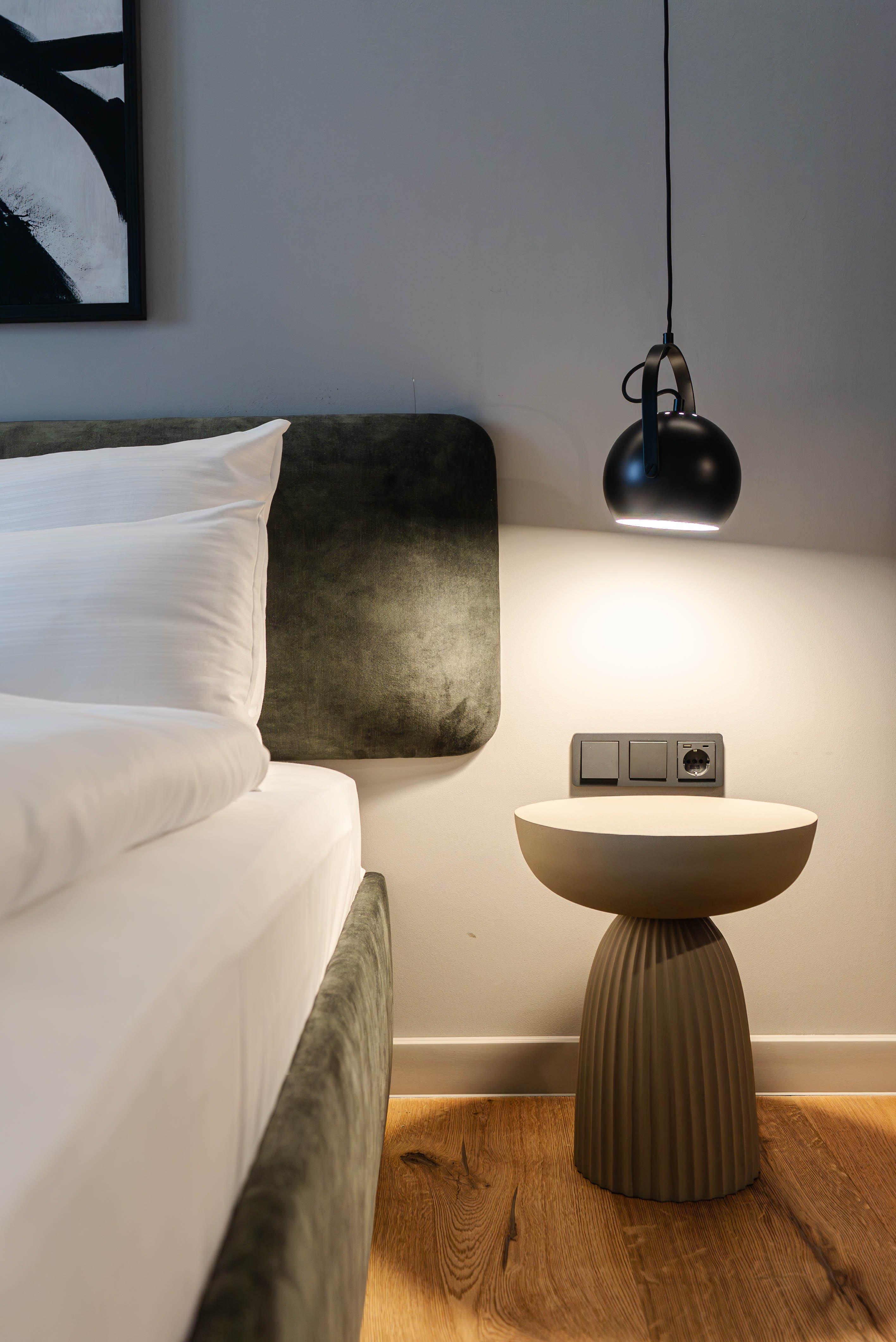 Lit avec tête de lit en velours, table d'appoint et lampe suspendue au-dessus.