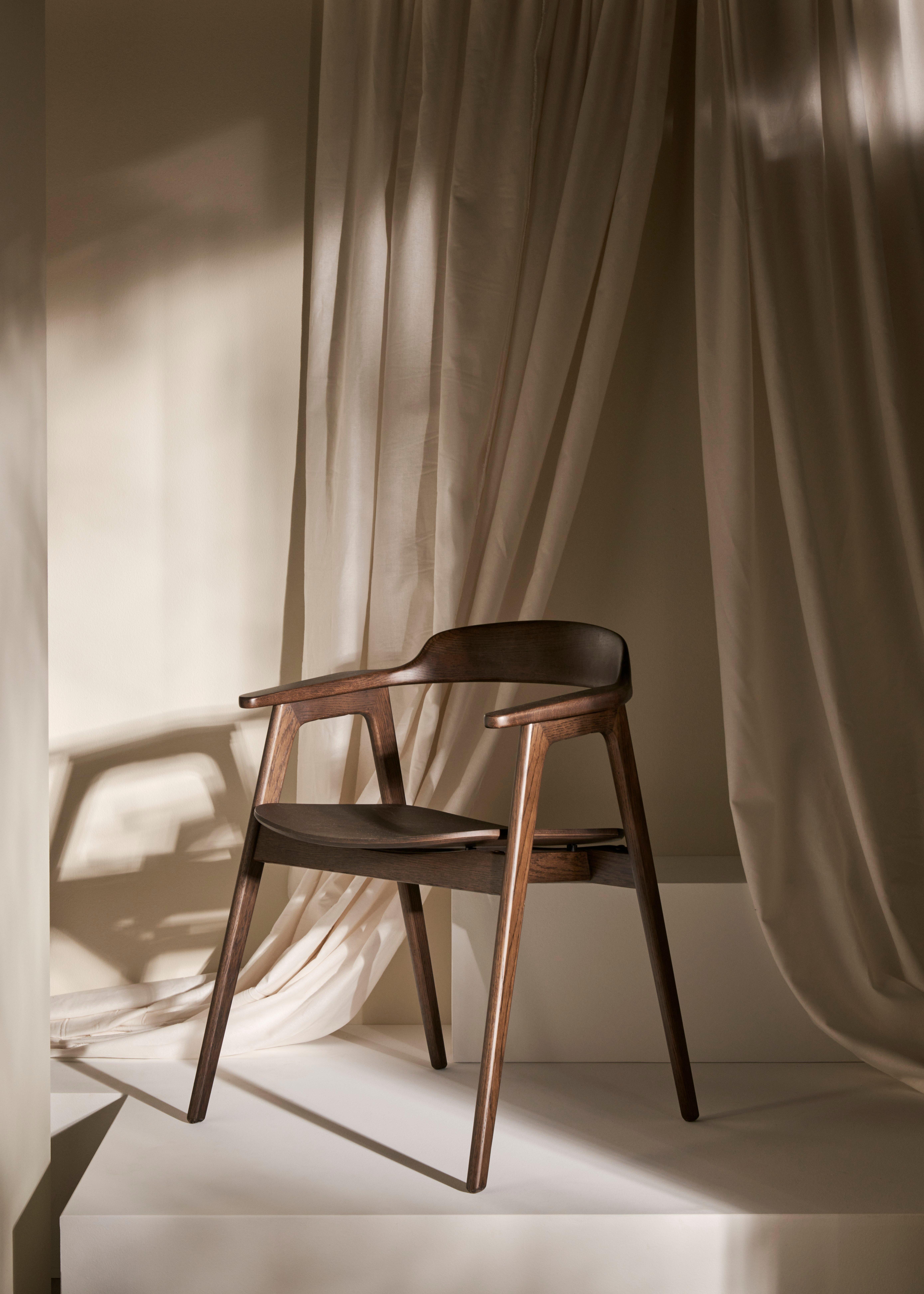 The Seoul dining chair in dark oak veneer is set against beige draped curtains, casting soft shadows in a warmly lit space.