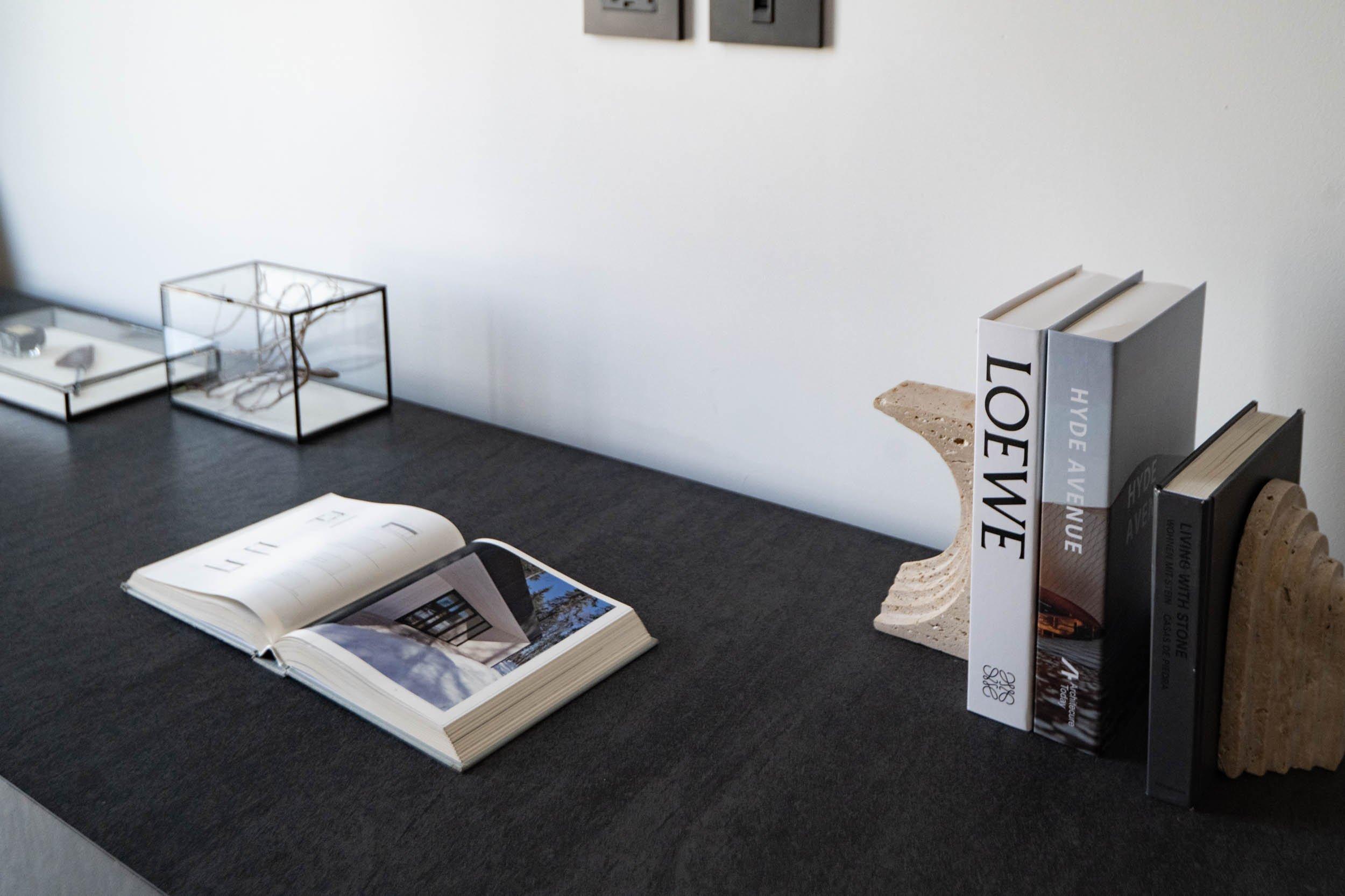 Livre ouvert et livres alignés entre deux serre-livres en pierre sur une table.