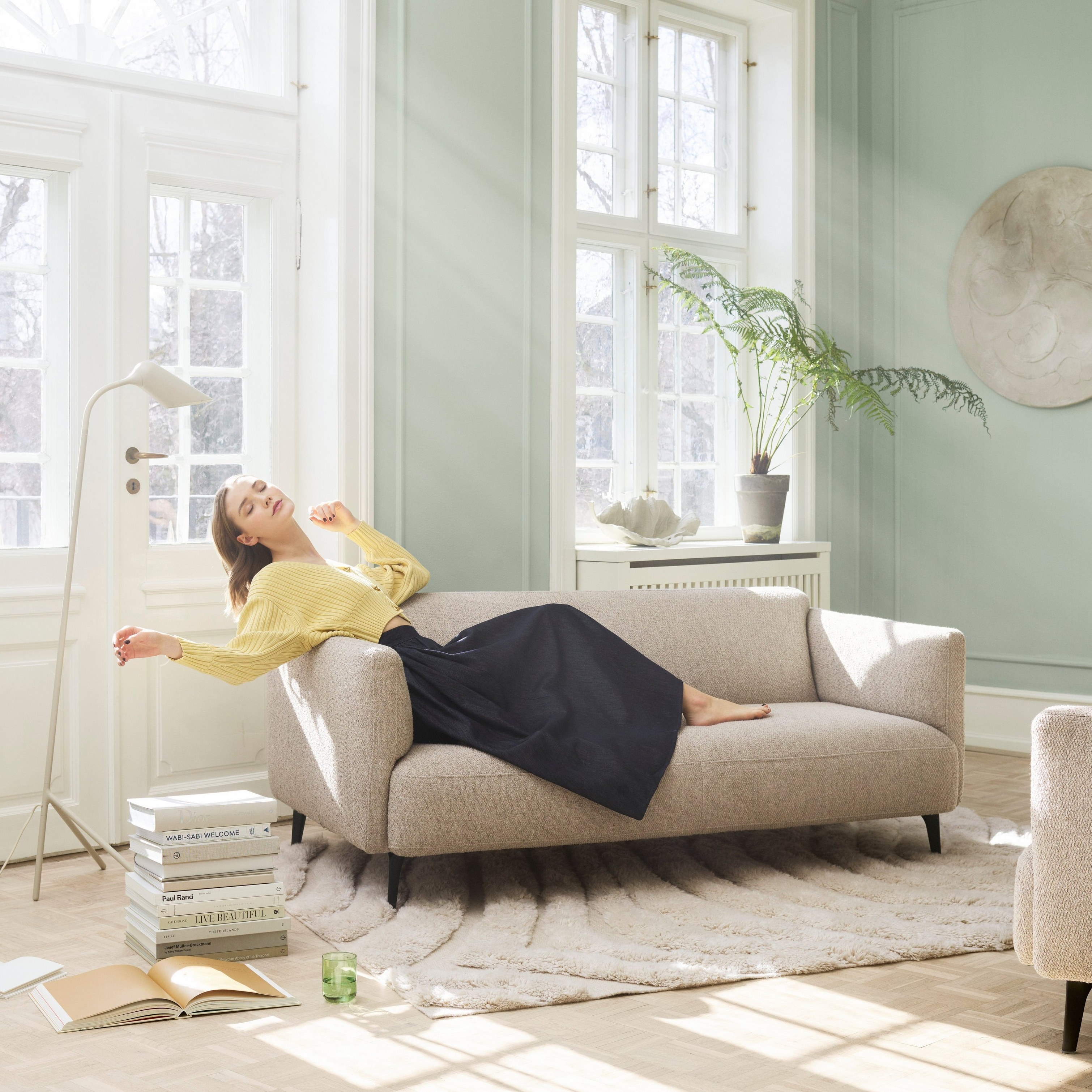 Woman lounging on the Modena sofa in a light-filled living room.