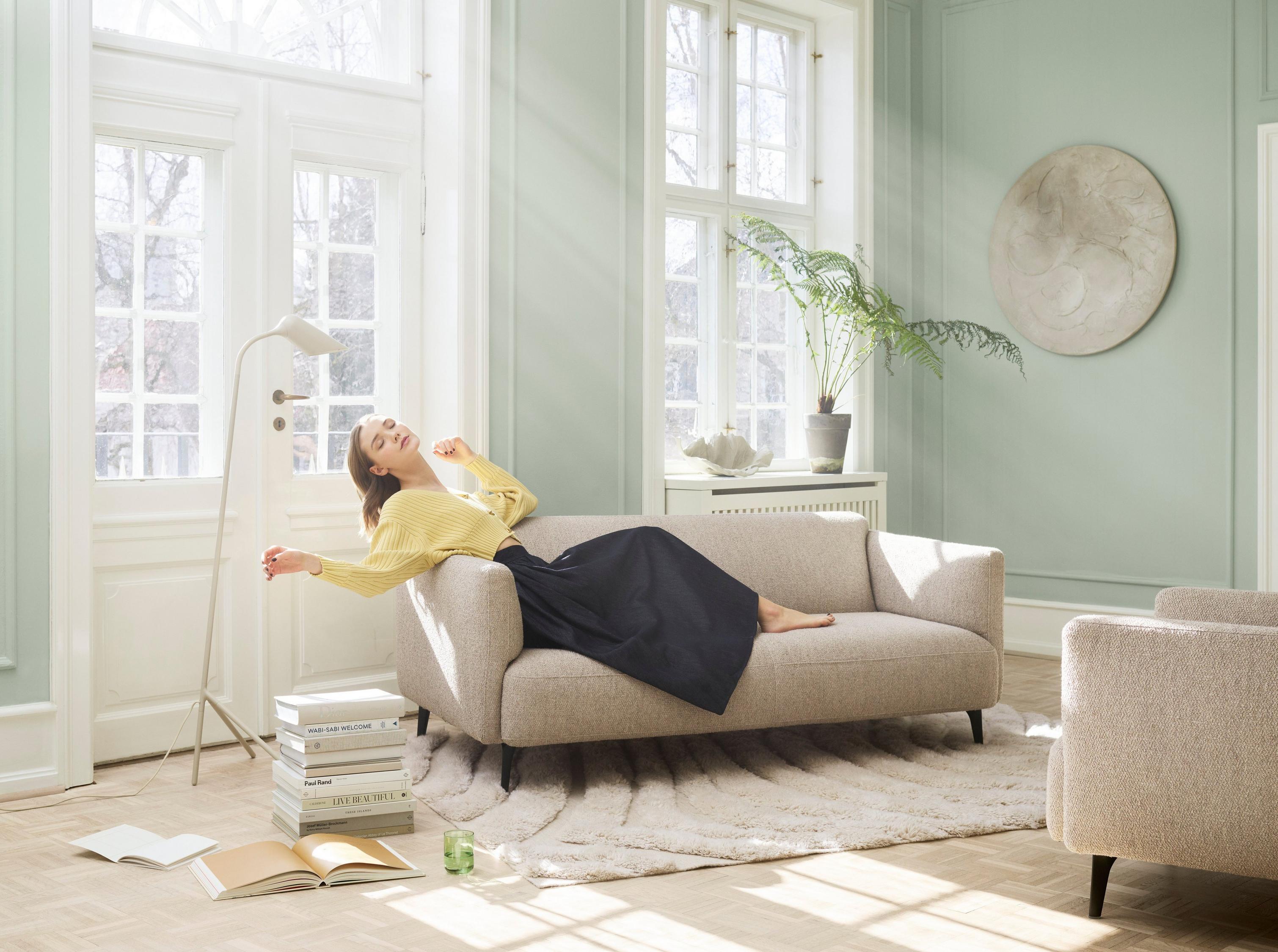 Woman lounging on the Modena sofa in a light-filled living room.