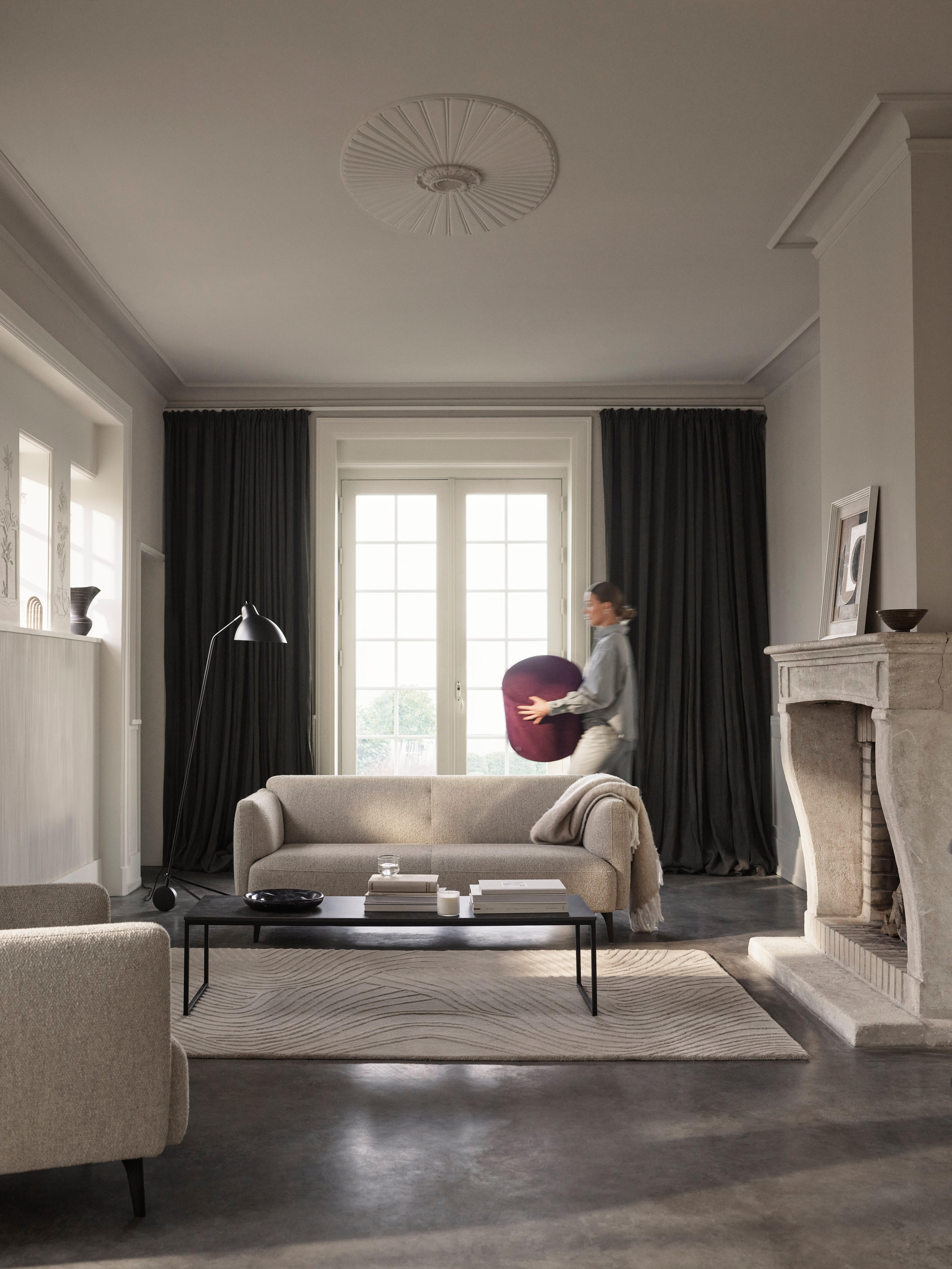 Cozy living room with Modena sofa and armchair in boucle fabric, where a woman is walking through with a purple pouffe