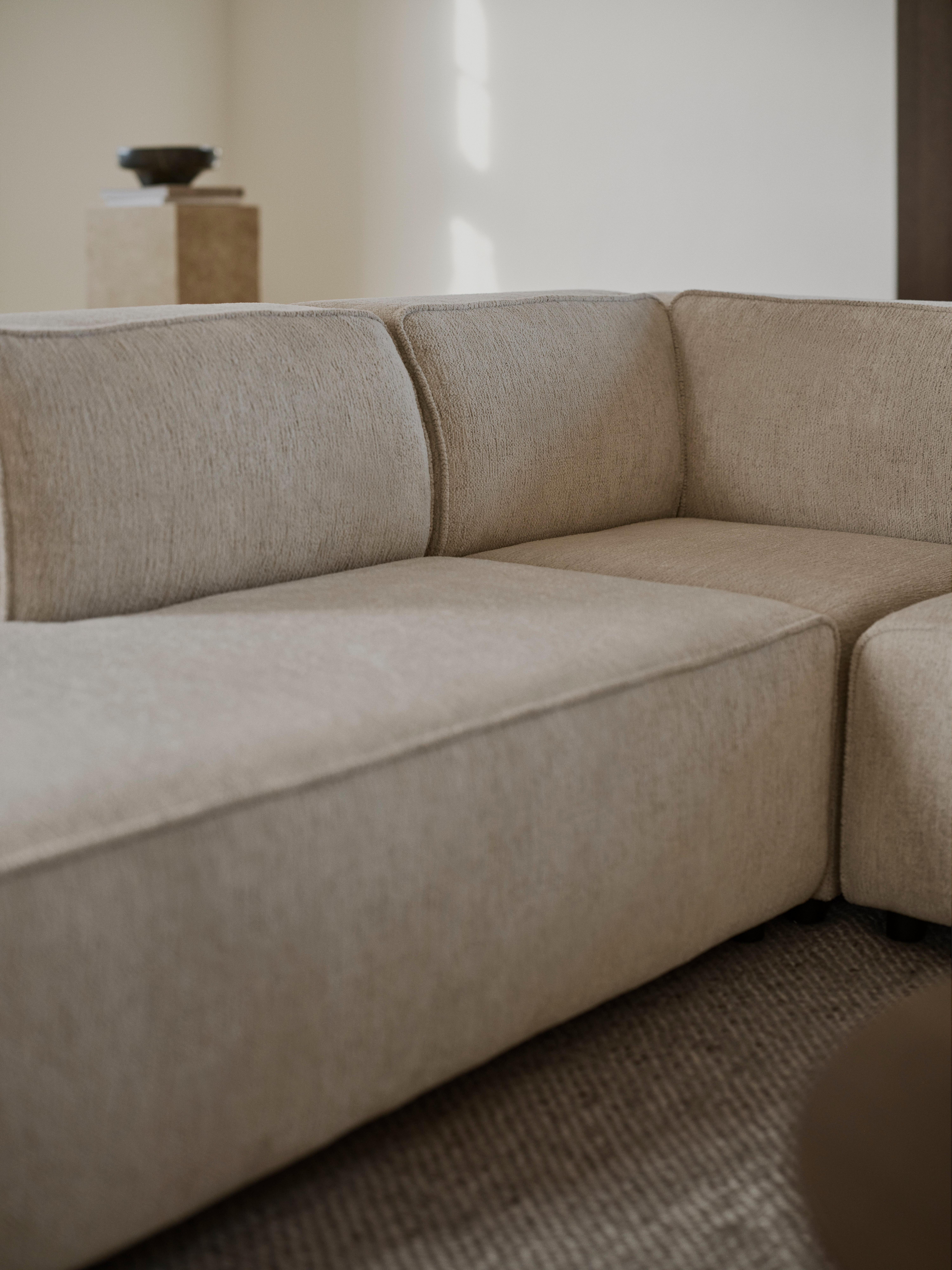 Nahaufnahme eines beigen Ecksofas mit Stoffbezug und gepolsterten Sitz- und Rückenkissen.