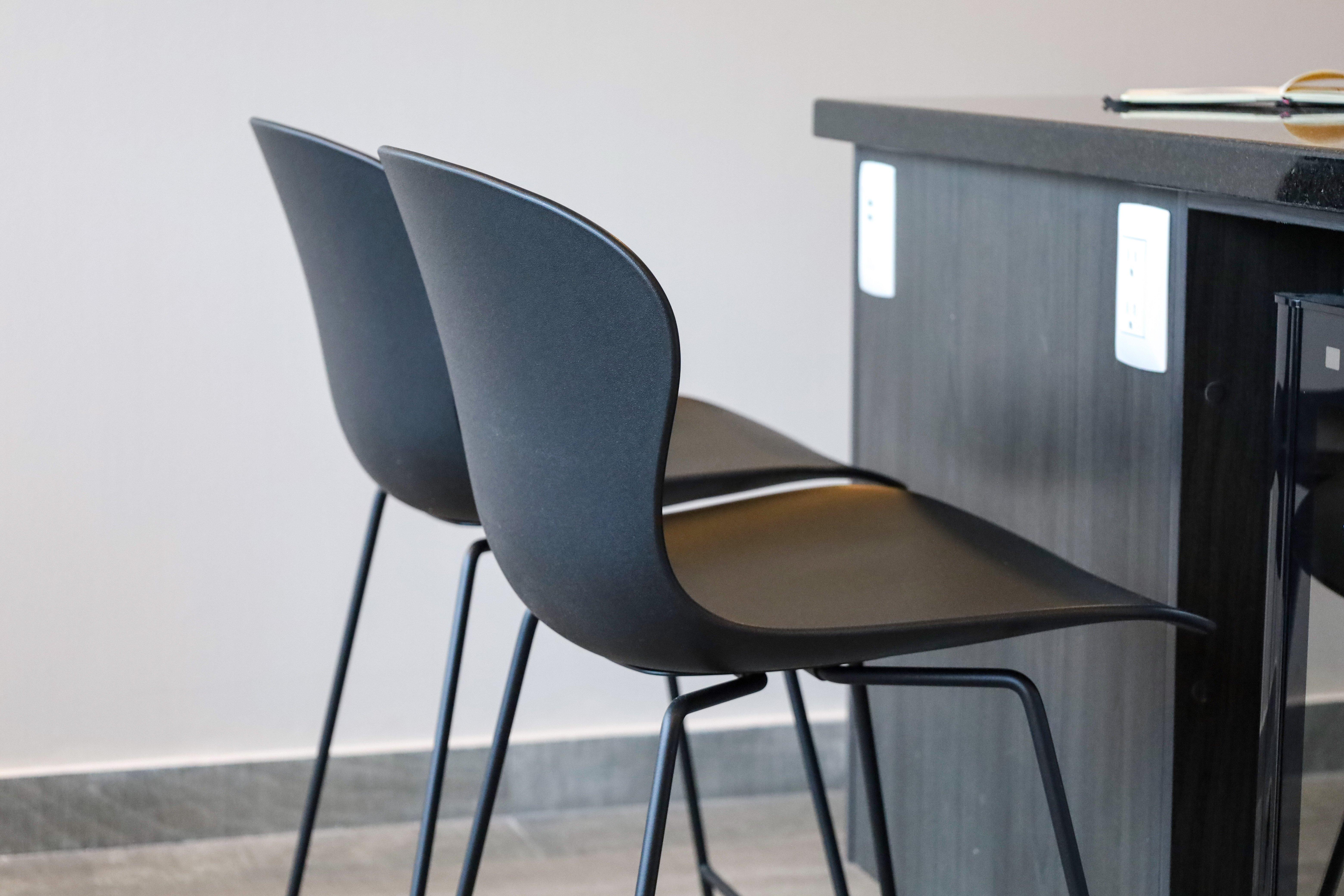 Two black bar stools with metal legs near a countertop with a notebook.