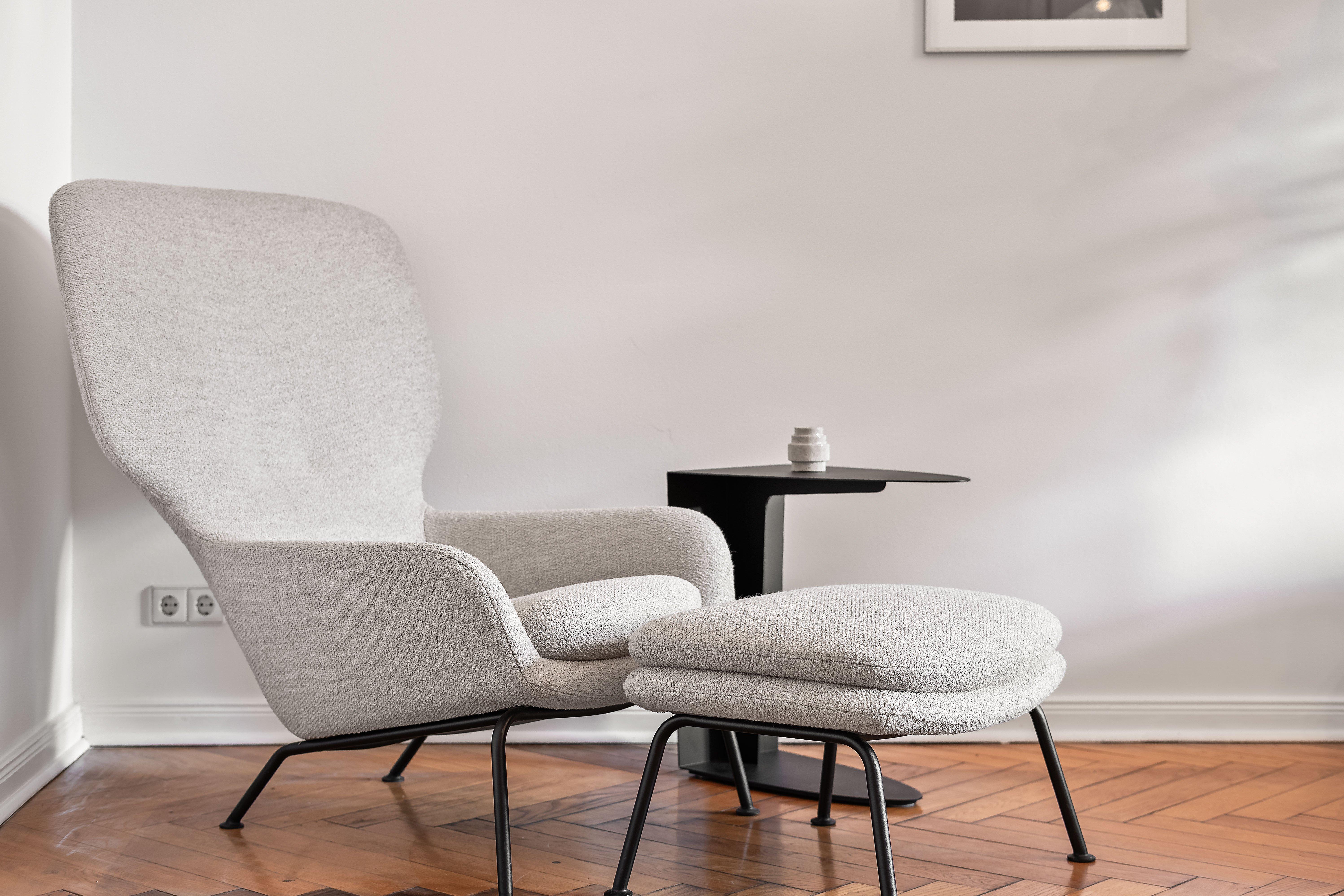 Fauteuil gris avec repose-pieds, table noire et petit vase sur parquet.