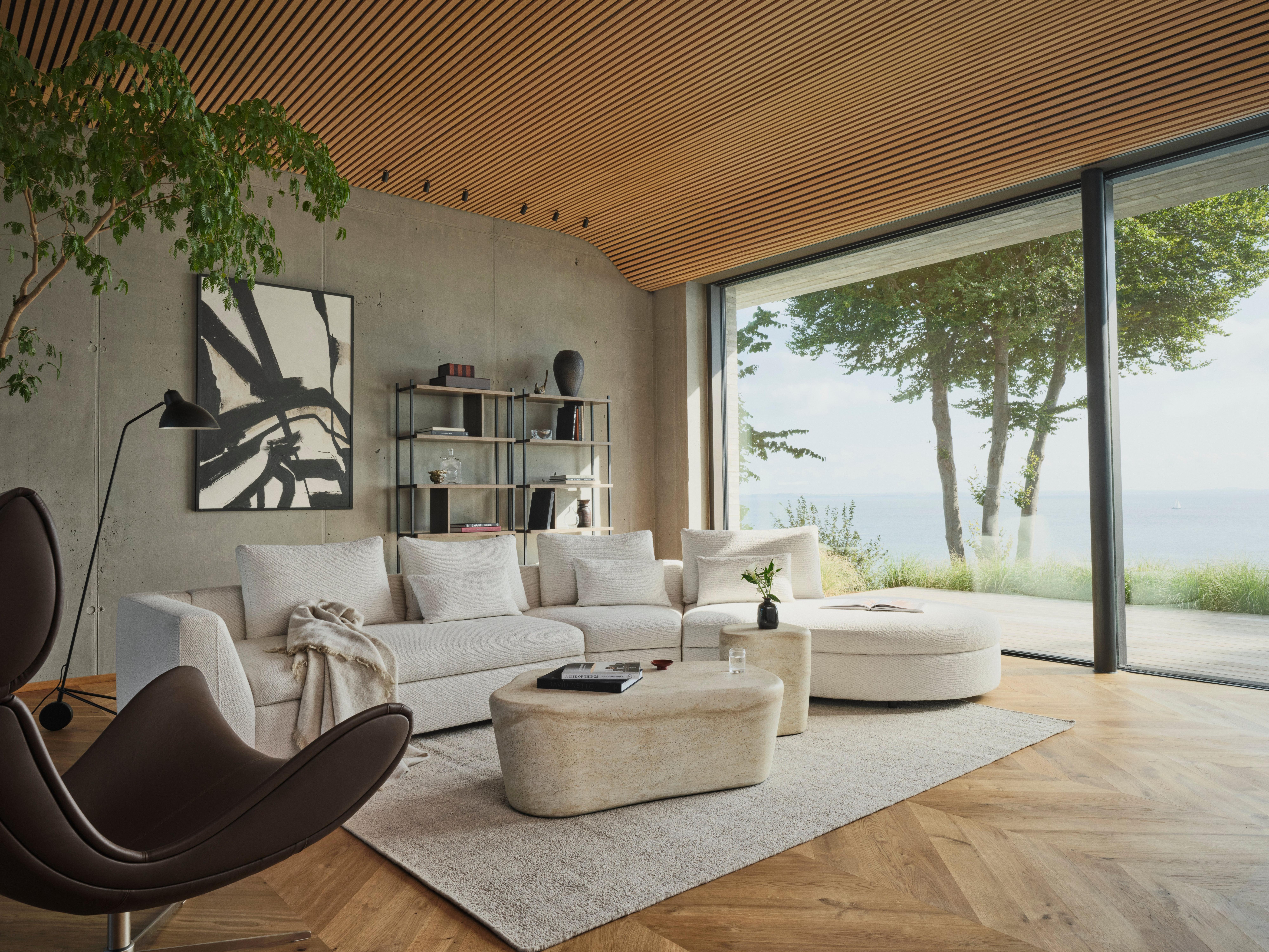 Modern living room with a white sectional Bergamo sofa, sculptural Terracina tables, Indivi armchair, and large windows overlooking the ocean.