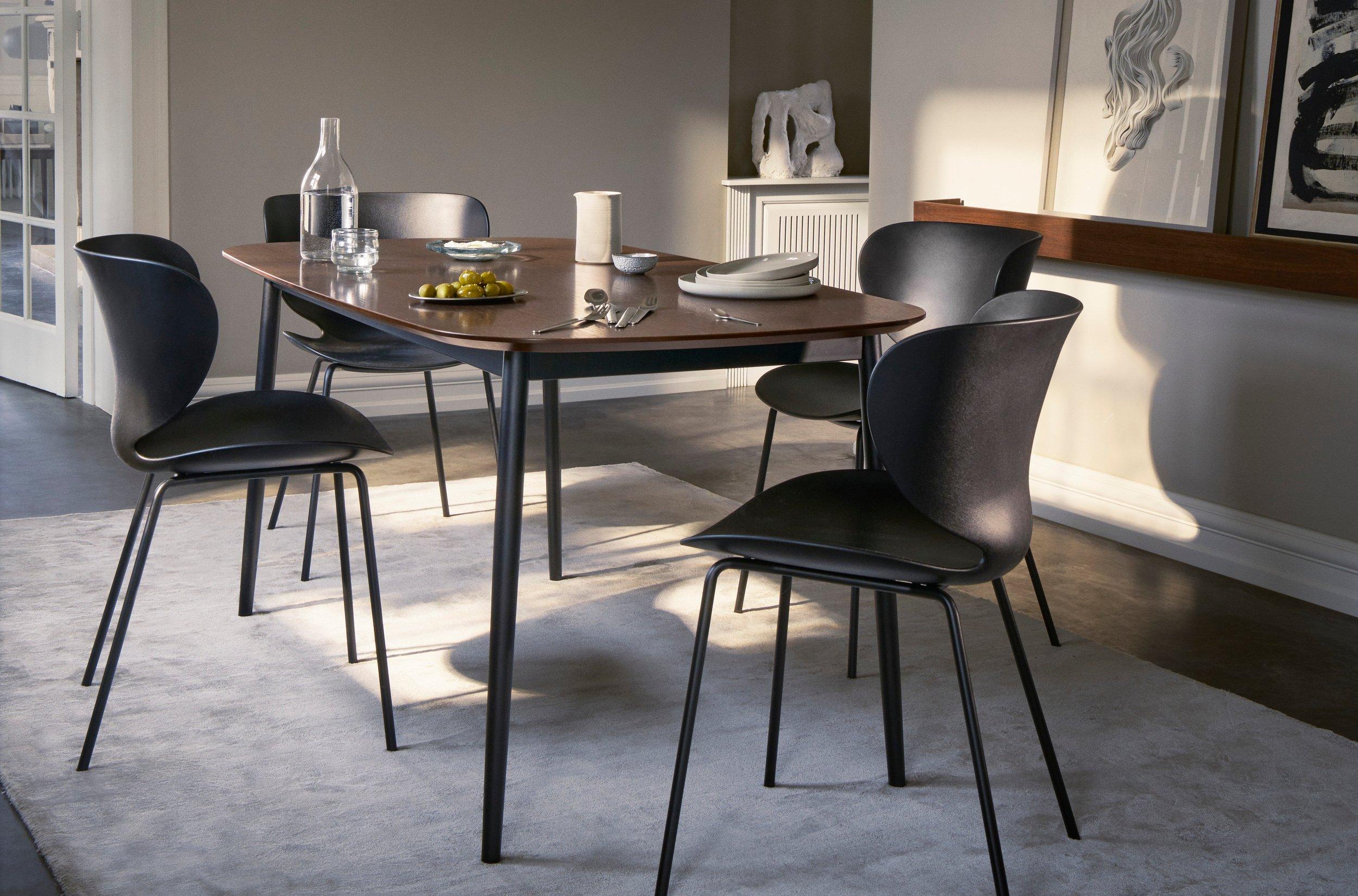 Kis, kerek Bornholm dohányzóasztal két fehér Hamilton székkel bézs függőlámpa alatt, könyvespolc és kék kanapé mellett, modern belső térben.