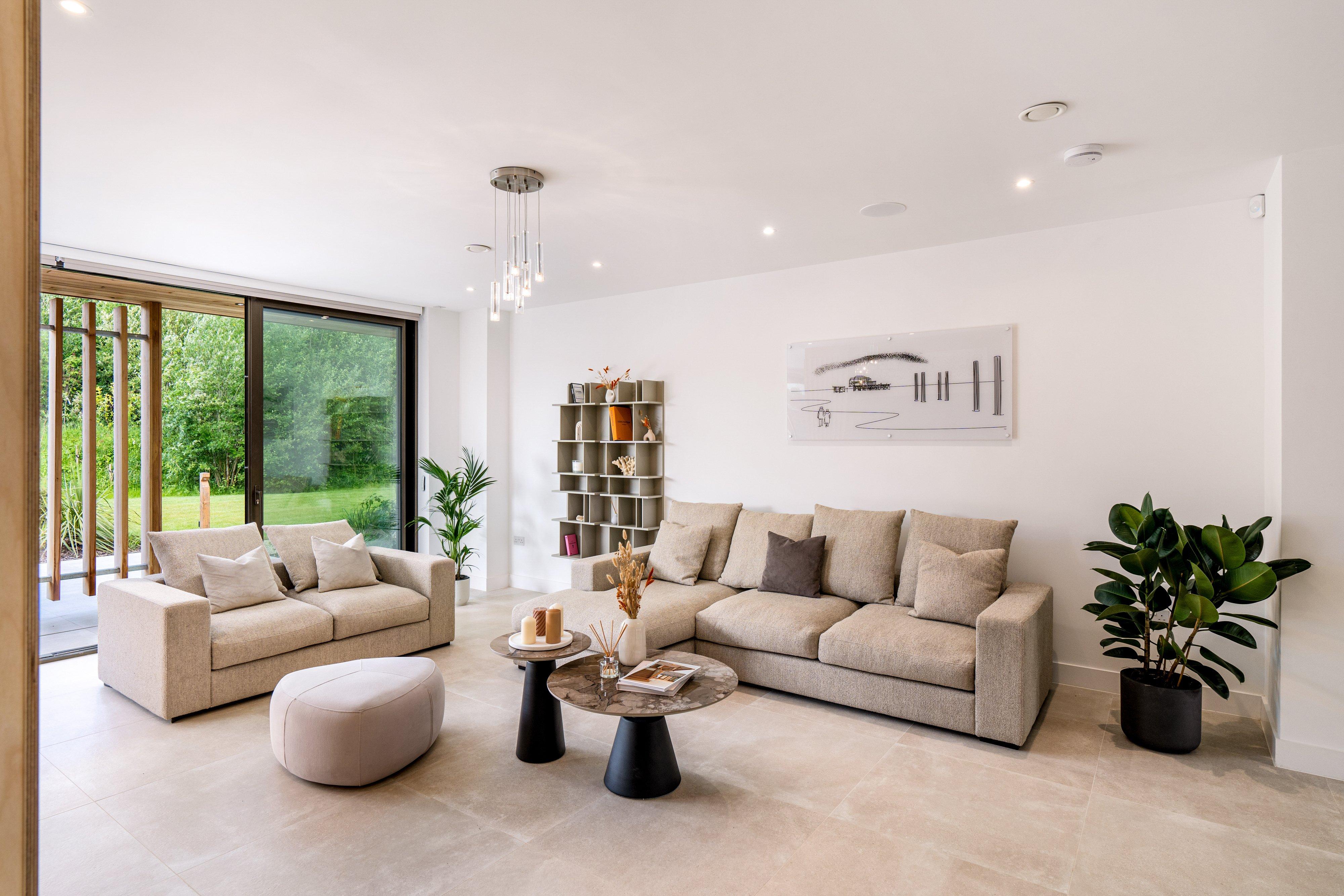 Modern living room with two beige sofas, nested coffee tables, and large sliding glass doors.