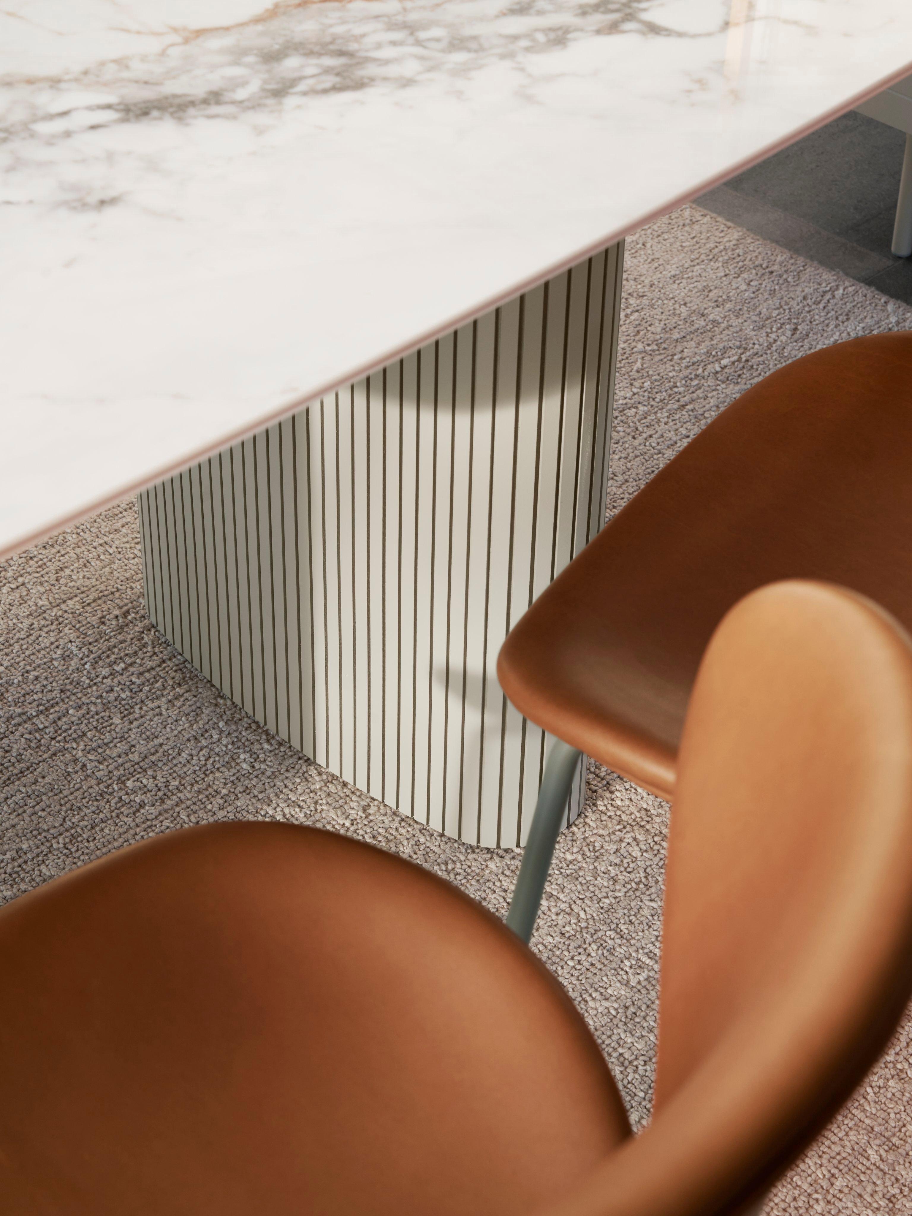 Marble table with striped base, surrounded by two brown chairs on carpet.