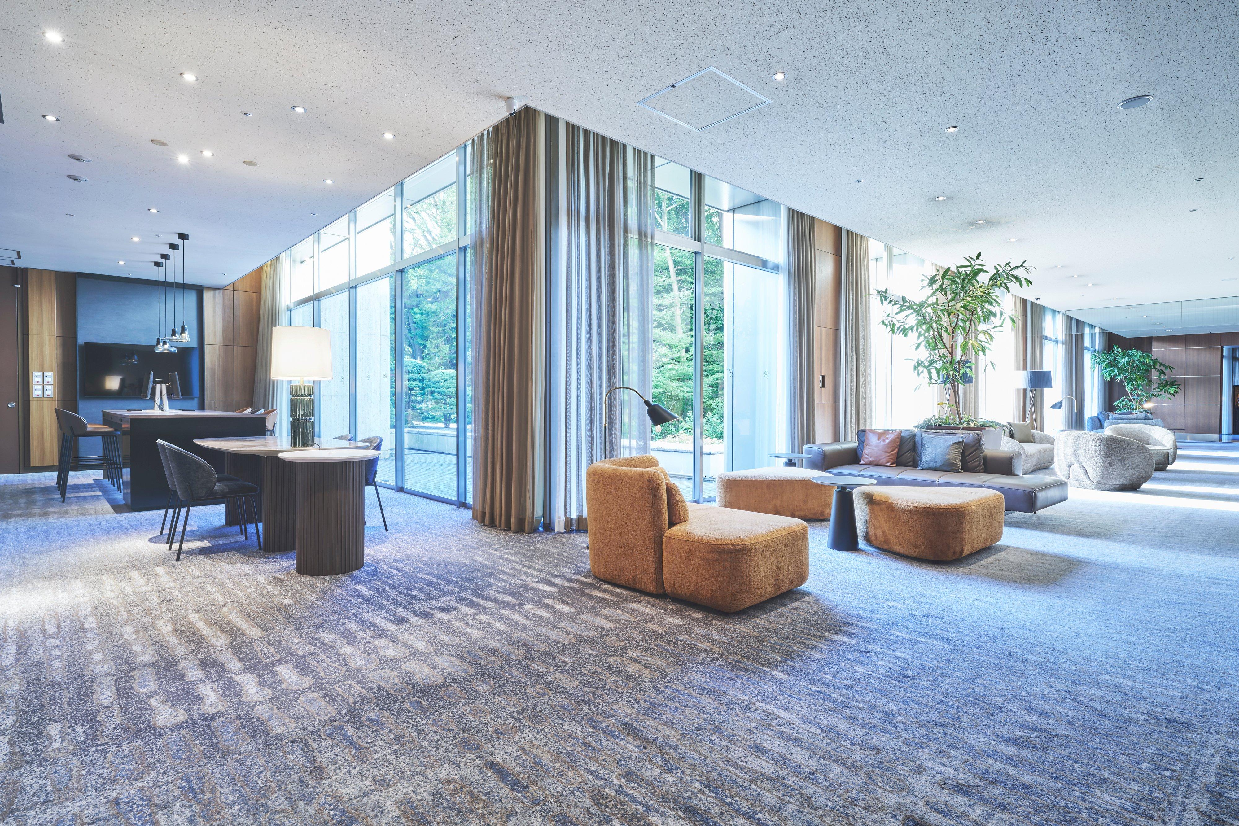 Modern lounge with sofas, ottomans and tables beside floor-to-ceiling windows.