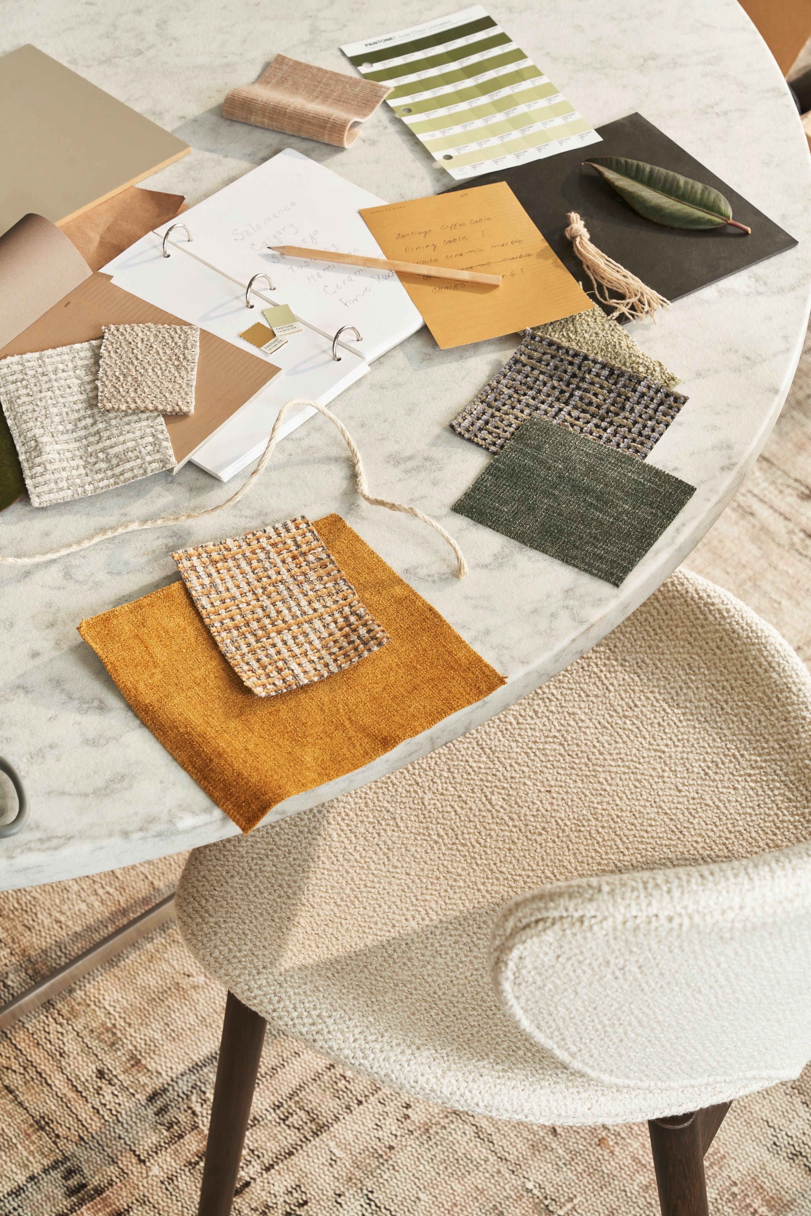 Marble table with fabric swatches, note cards, and pencil in natural tones.