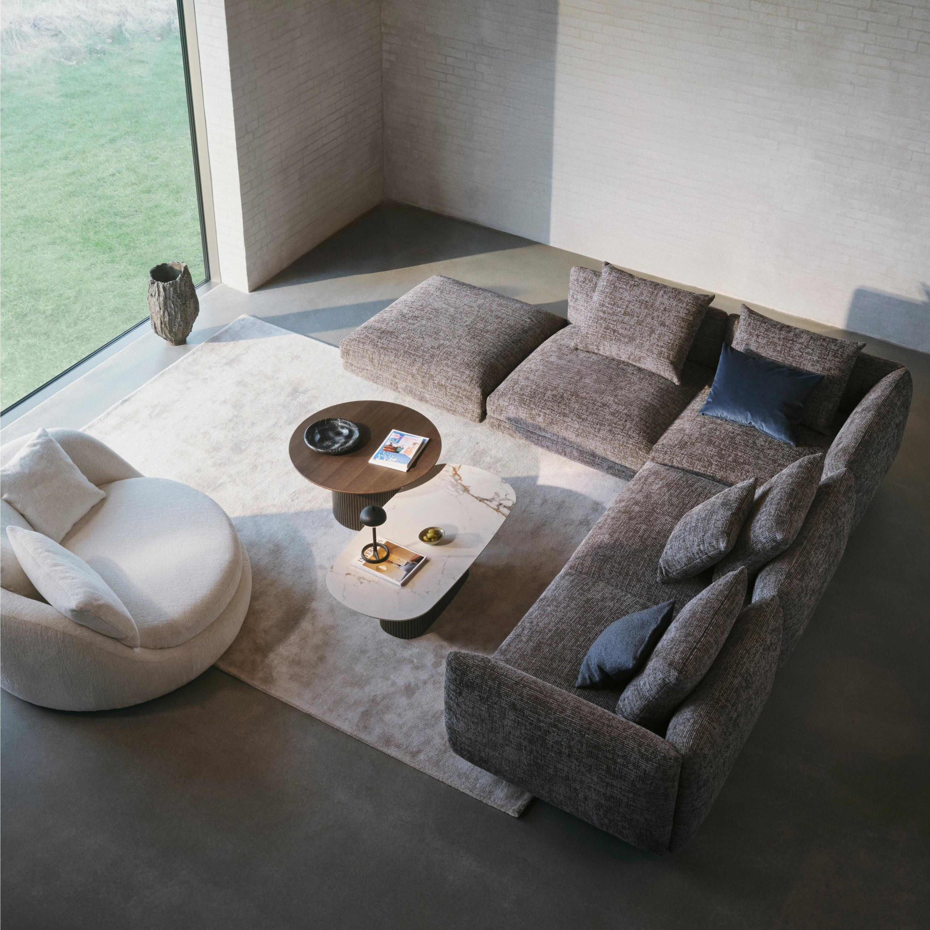 Modern living room with a textured grey sectional, round white lounge chair, and nested tables on a light rug by a large window.