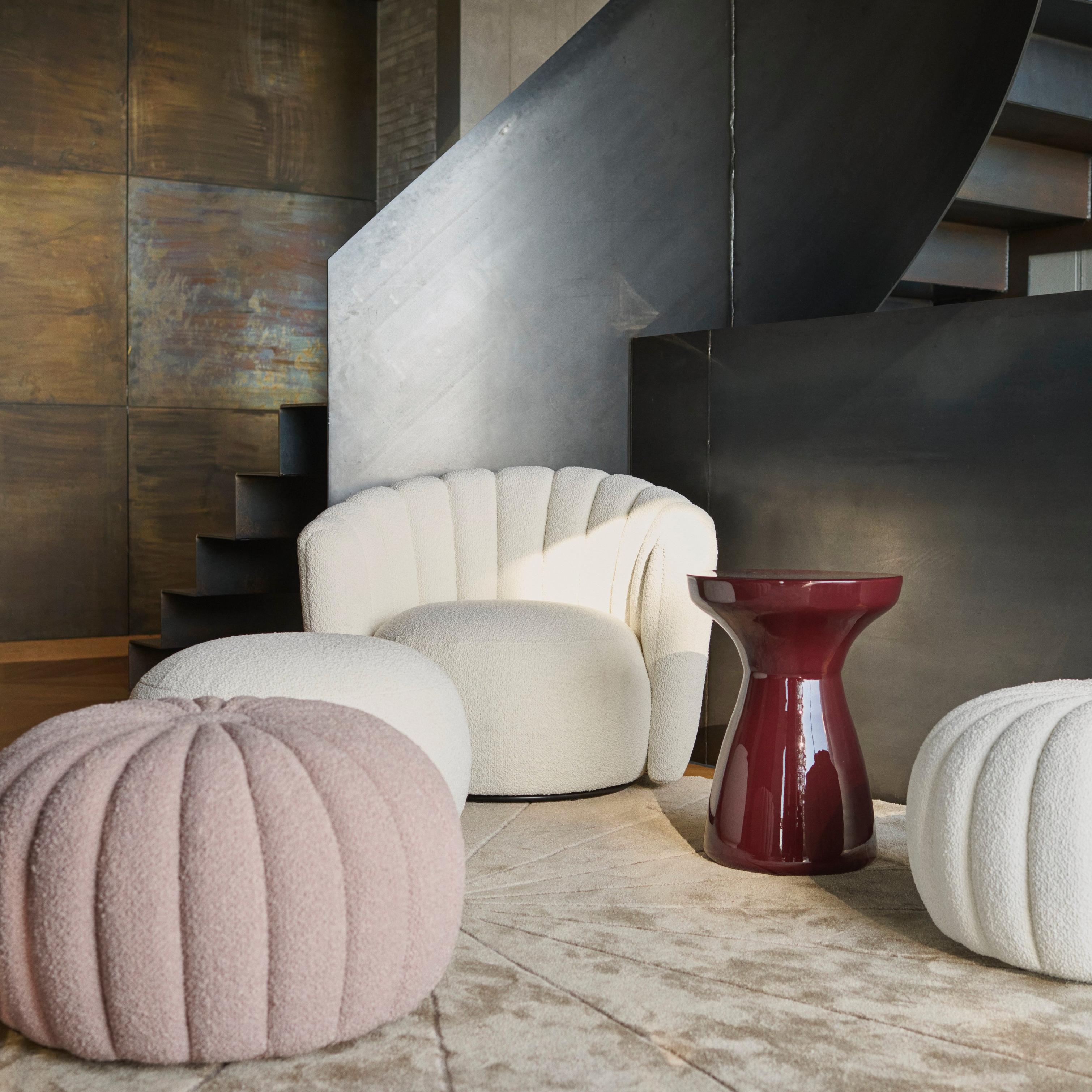Modern lounge with textured armchair, pouffes, and maroon side table on a round rug.