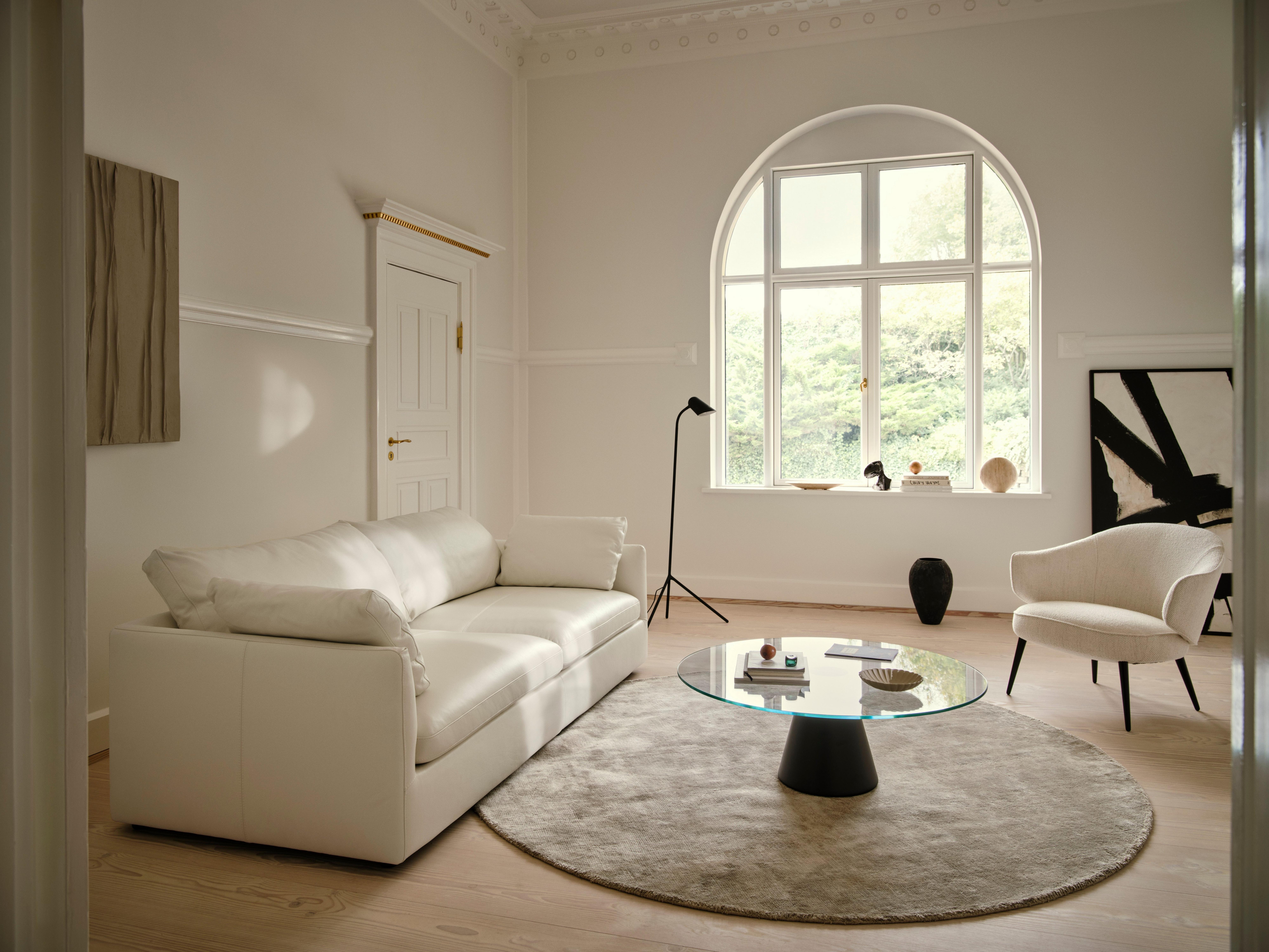 白いソファと椅子があるモダンなリビングルーム。大きな窓とガラステーブルが特徴。