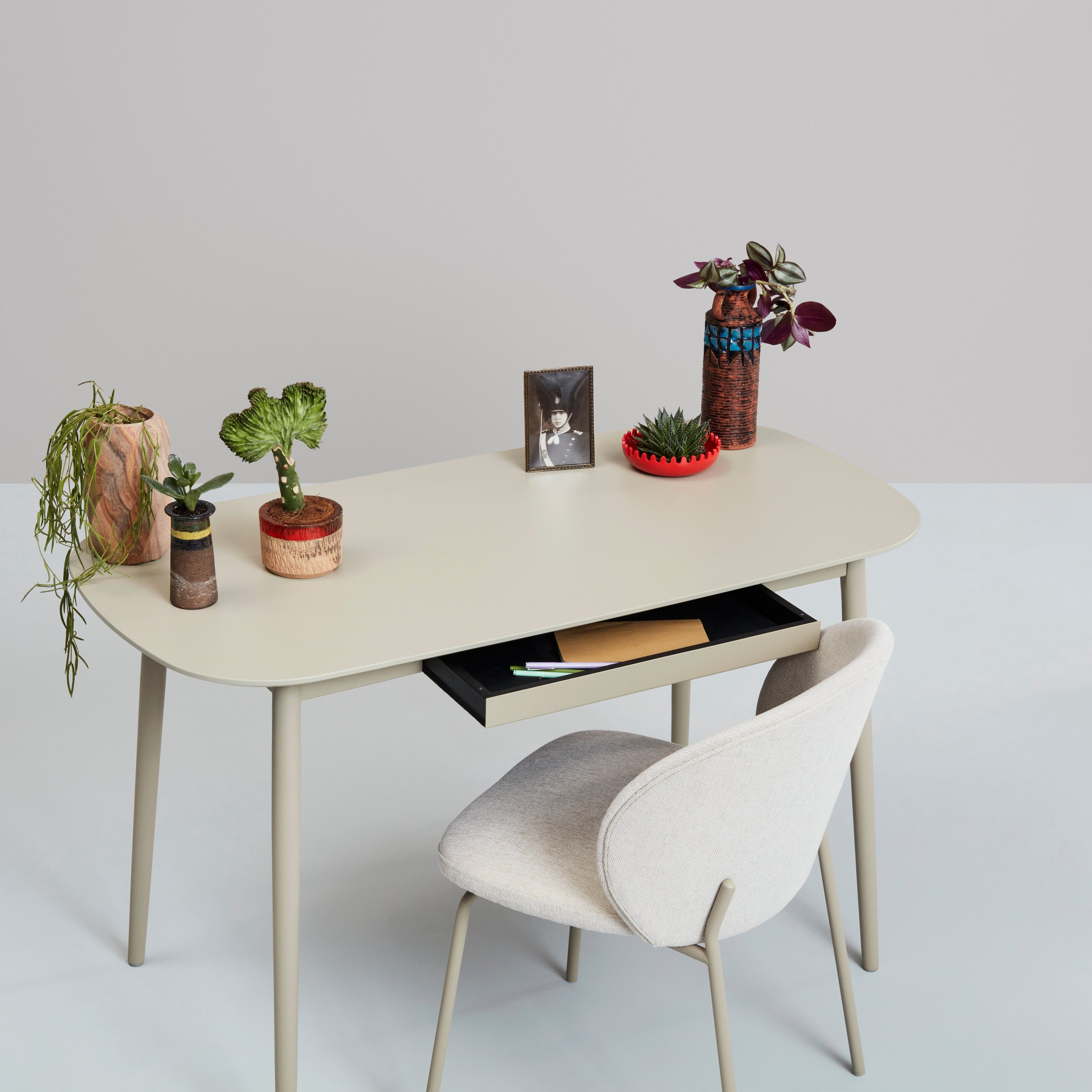 Vitt skrivbord med växter, dekorationer och en stol mot en neutral bakgrund.
