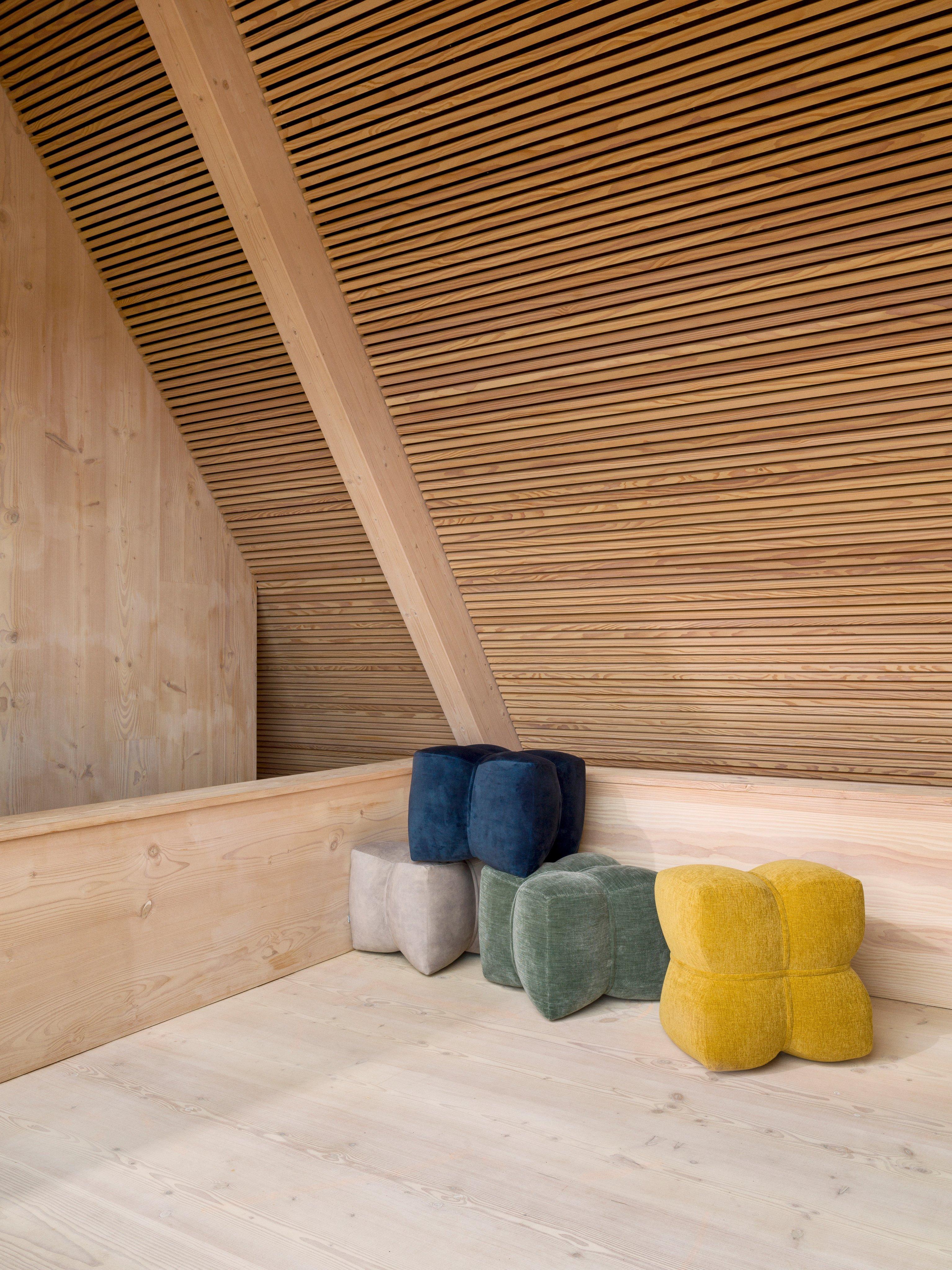 Several Nawabari pouffes upholstered in Ravello, Napoli and Tomelilla fabrics in the corner of a wooden room.