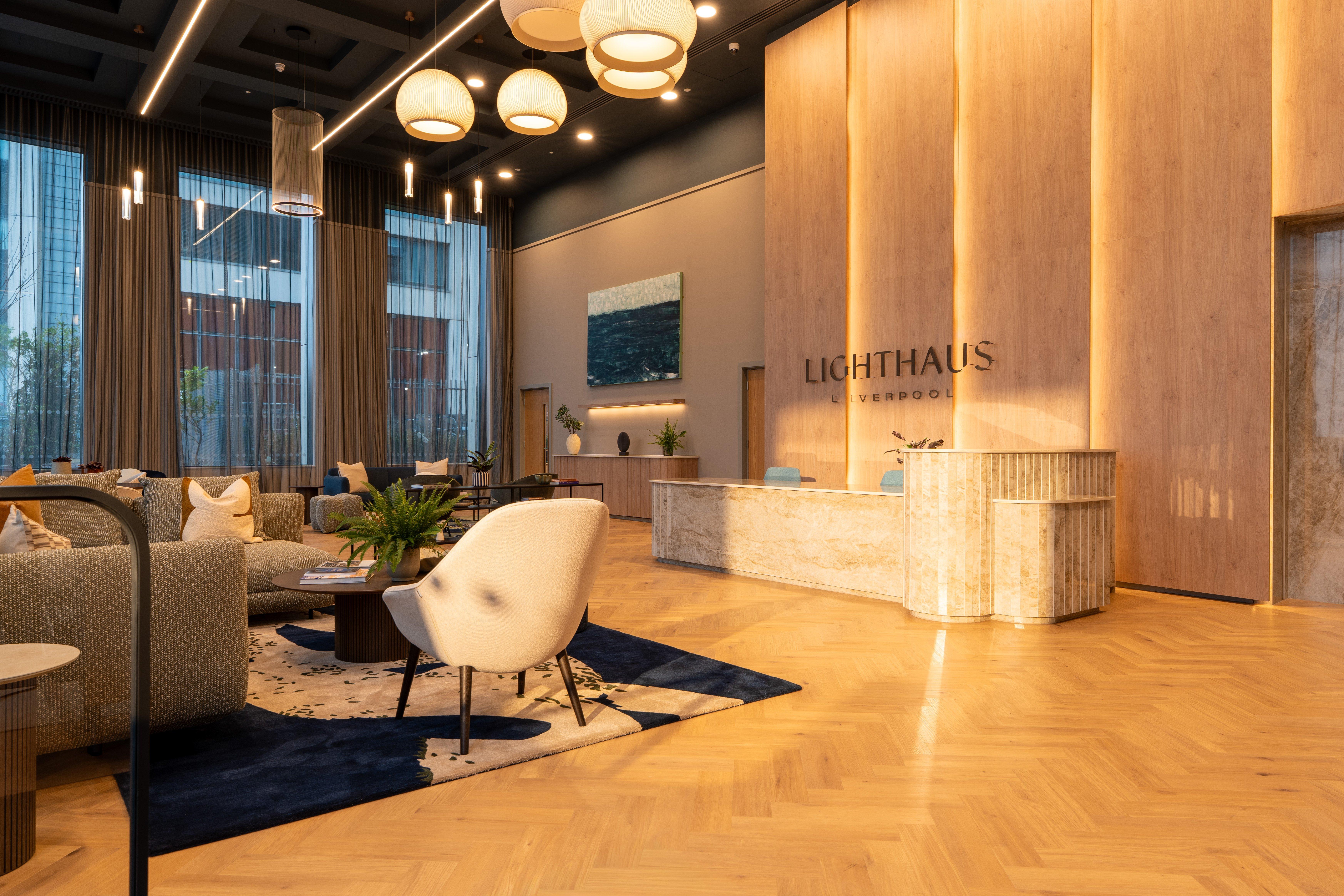 Modern hotel lobby recepciópulttal és ülőgarnitúrával, „LICHTHAUS LIVERPOOL” felirattal.