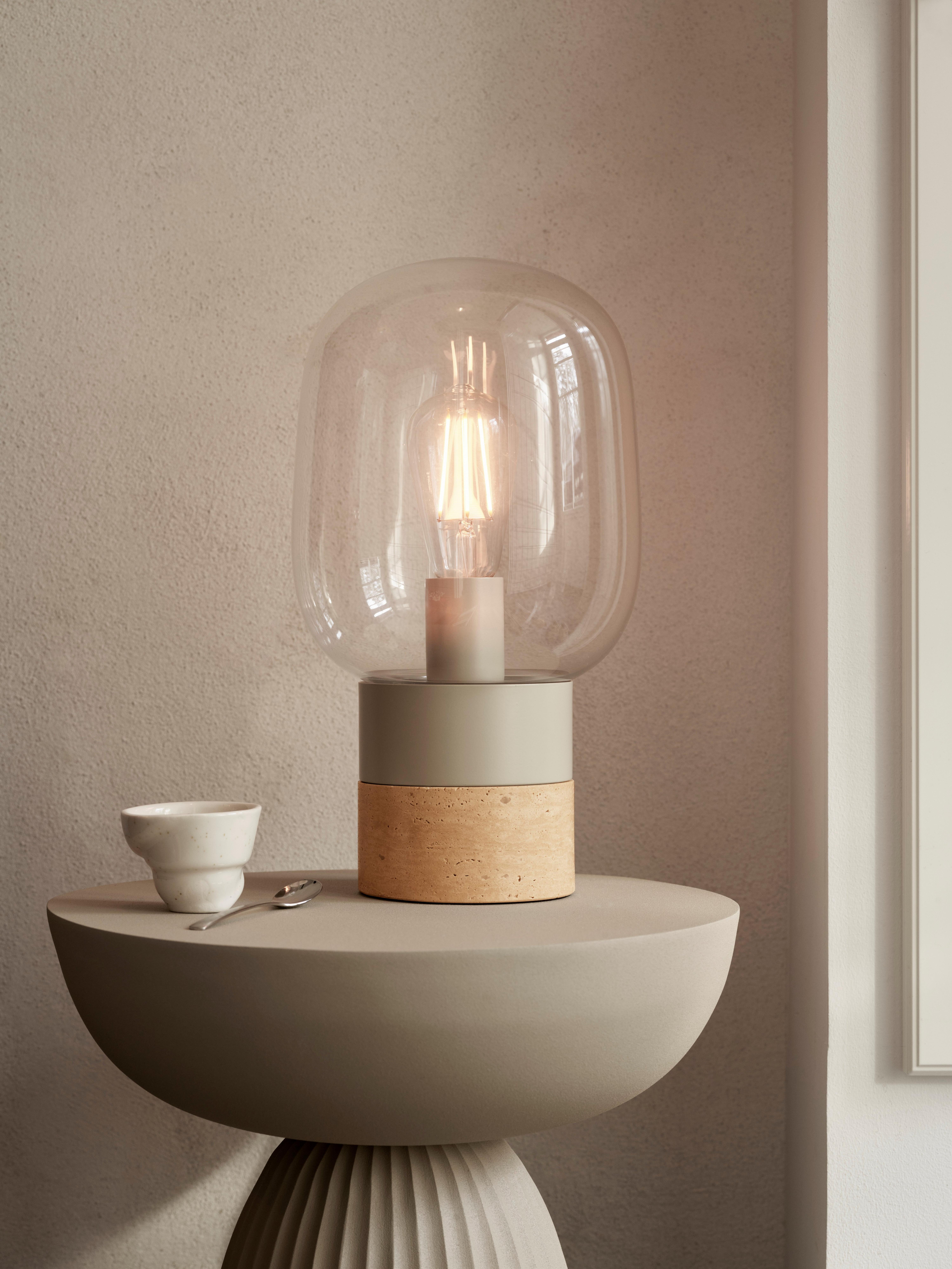 带有透明玻璃灯泡和米色底座的现代风台灯，放在圆形底座桌上，旁边是一个白色小杯子。