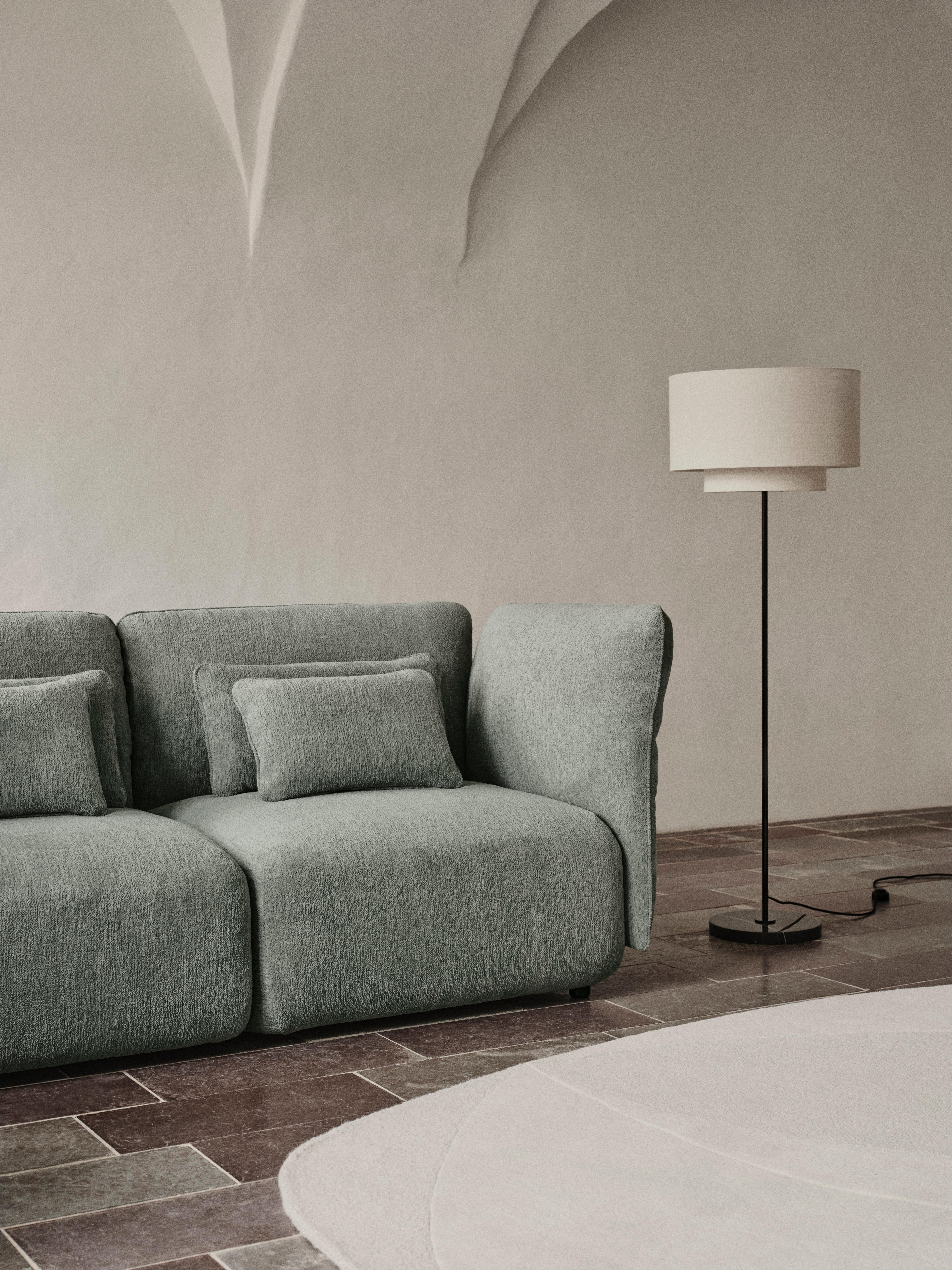 Grey fabric sofa with cushions next to a black floor lamp with a white shade.