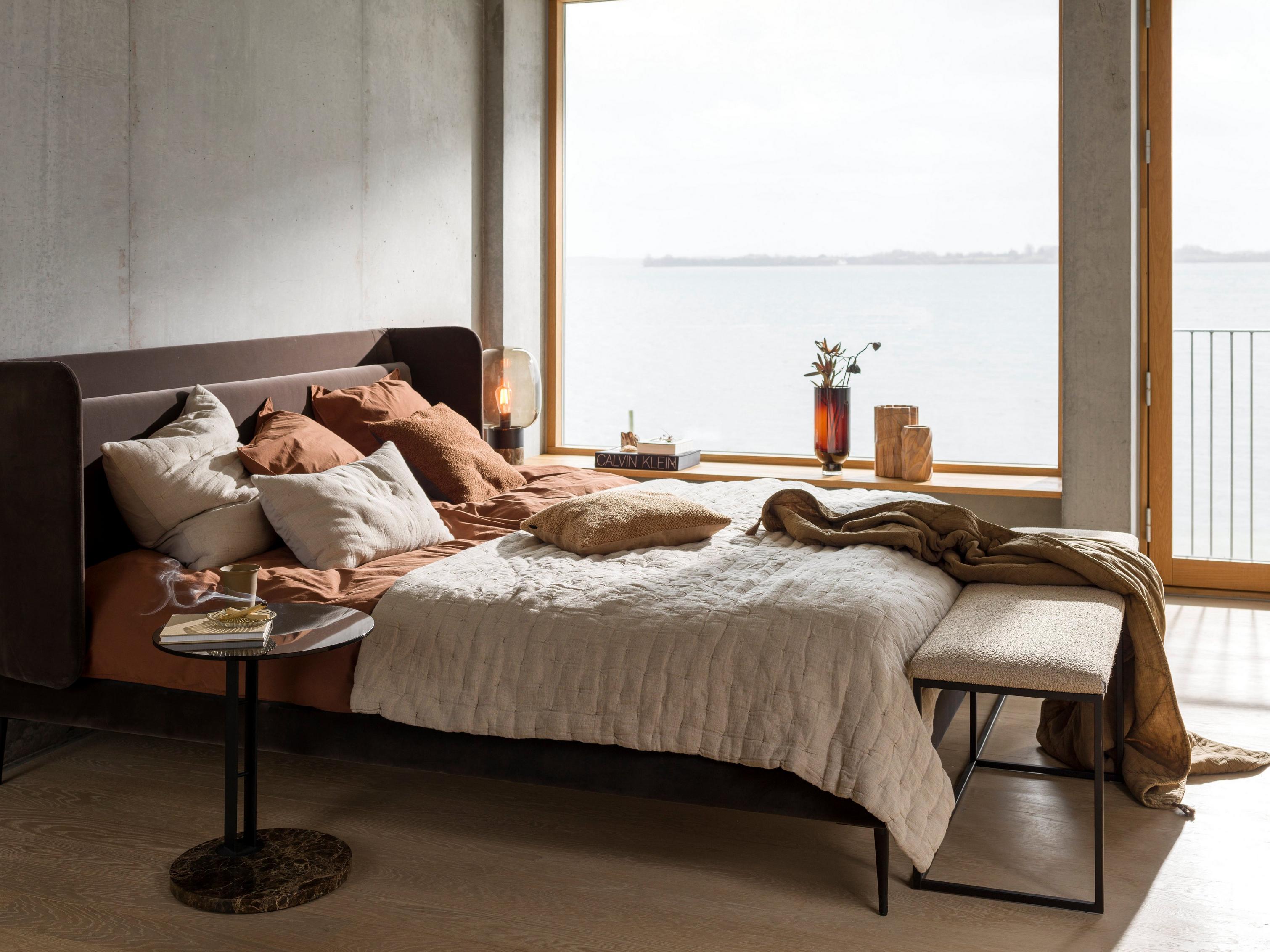 Cozy bedroom with a view of the water, featuring earth-toned bedding and a small side table.
