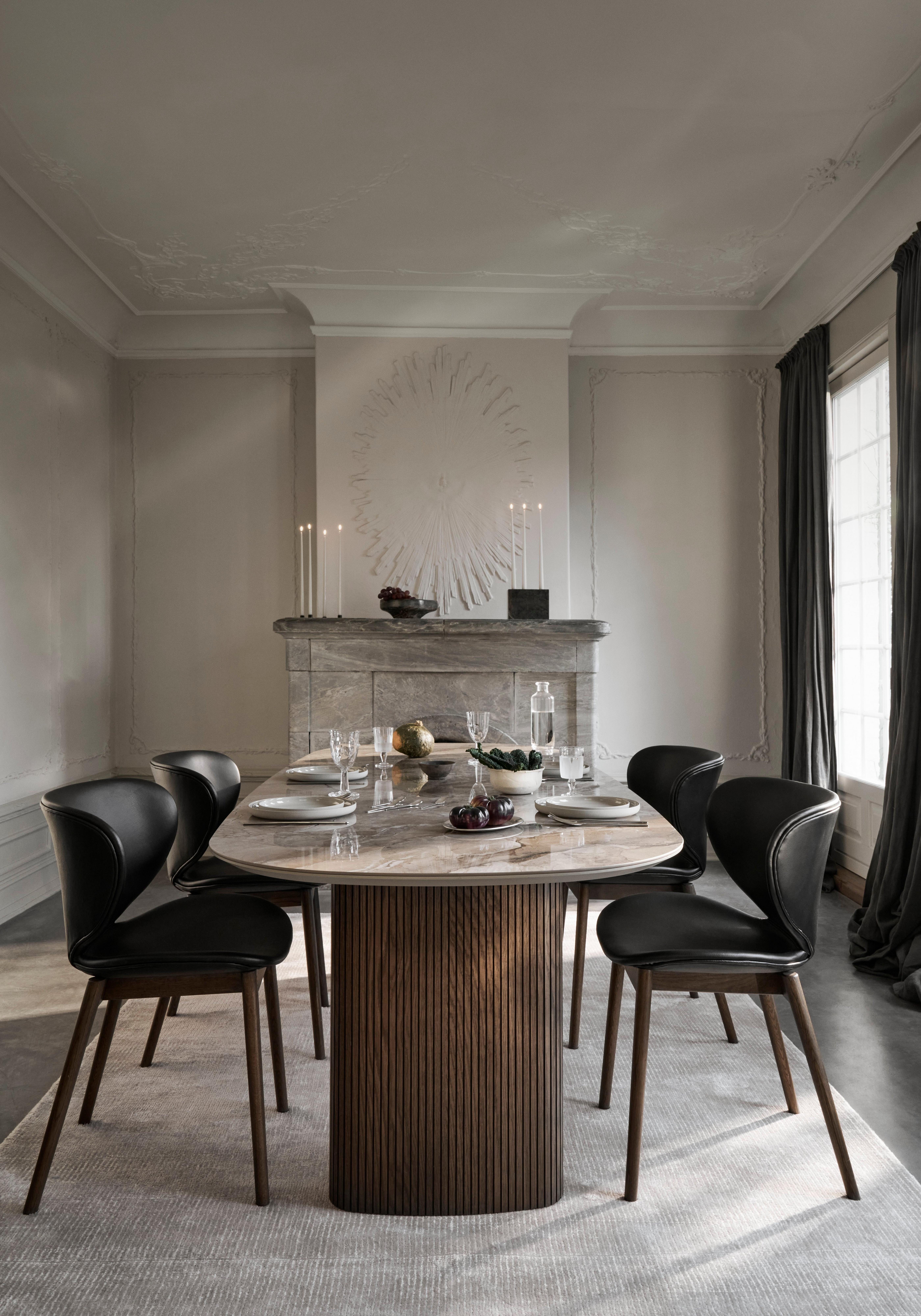 Dining room with a marble table, blue Adelaide chairs, a blue rug, a window, and a black shelf filled with books and decor.