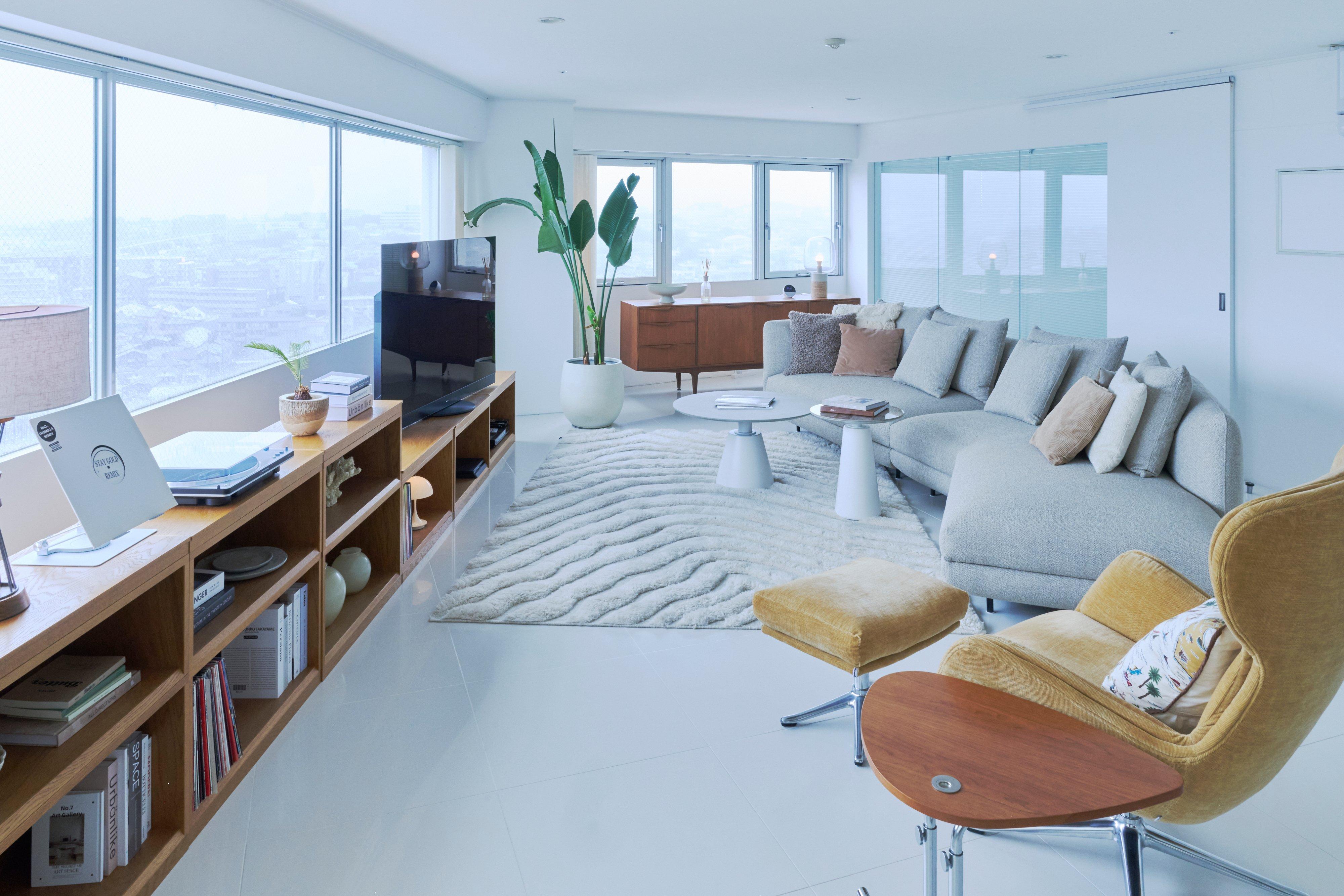 Modern living room with grey corner sofa, TV on wooden unit, and yellow chair with footstool.