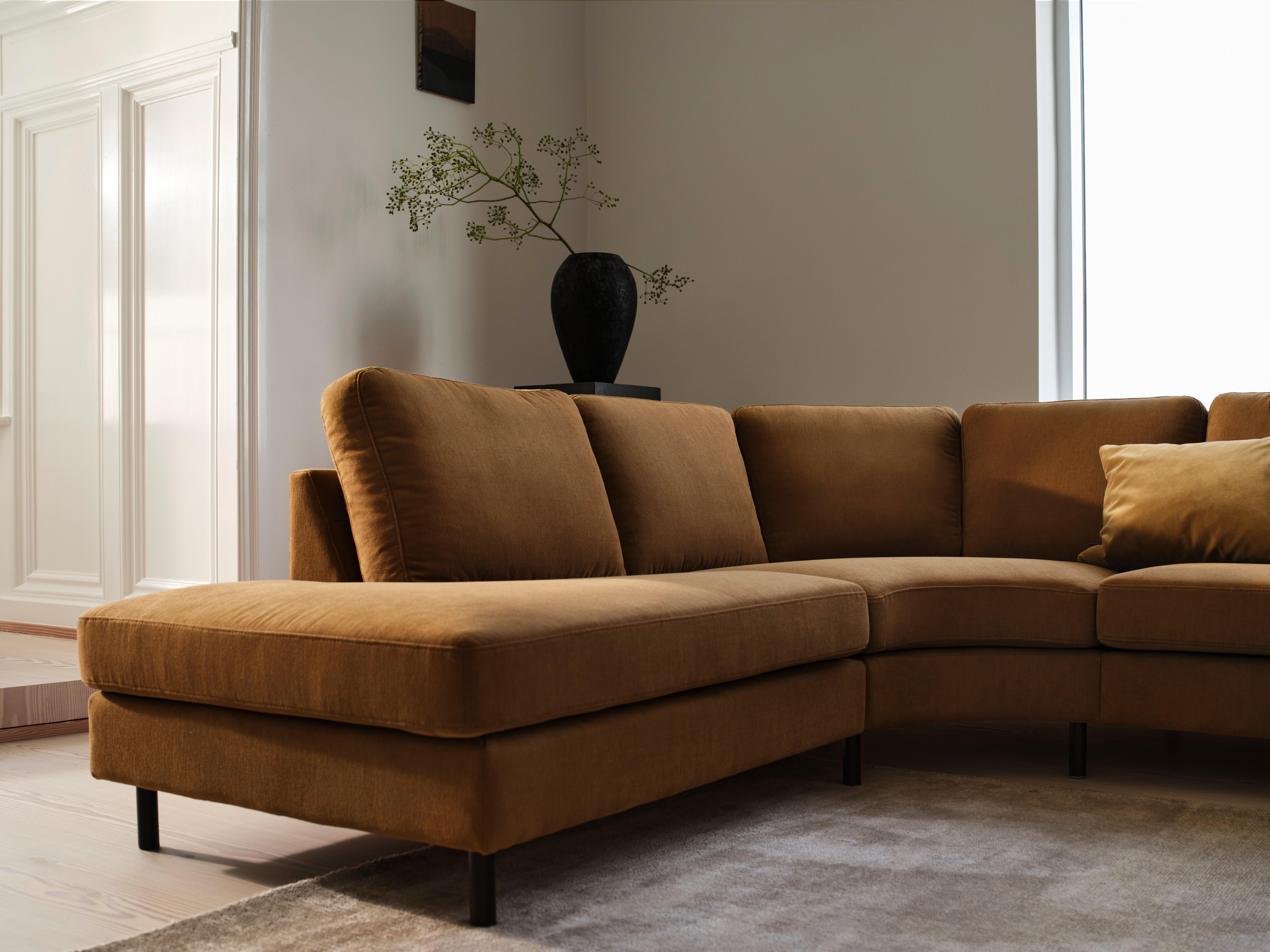 Brown corner sofa with cushions, black vase on table, plant decor.