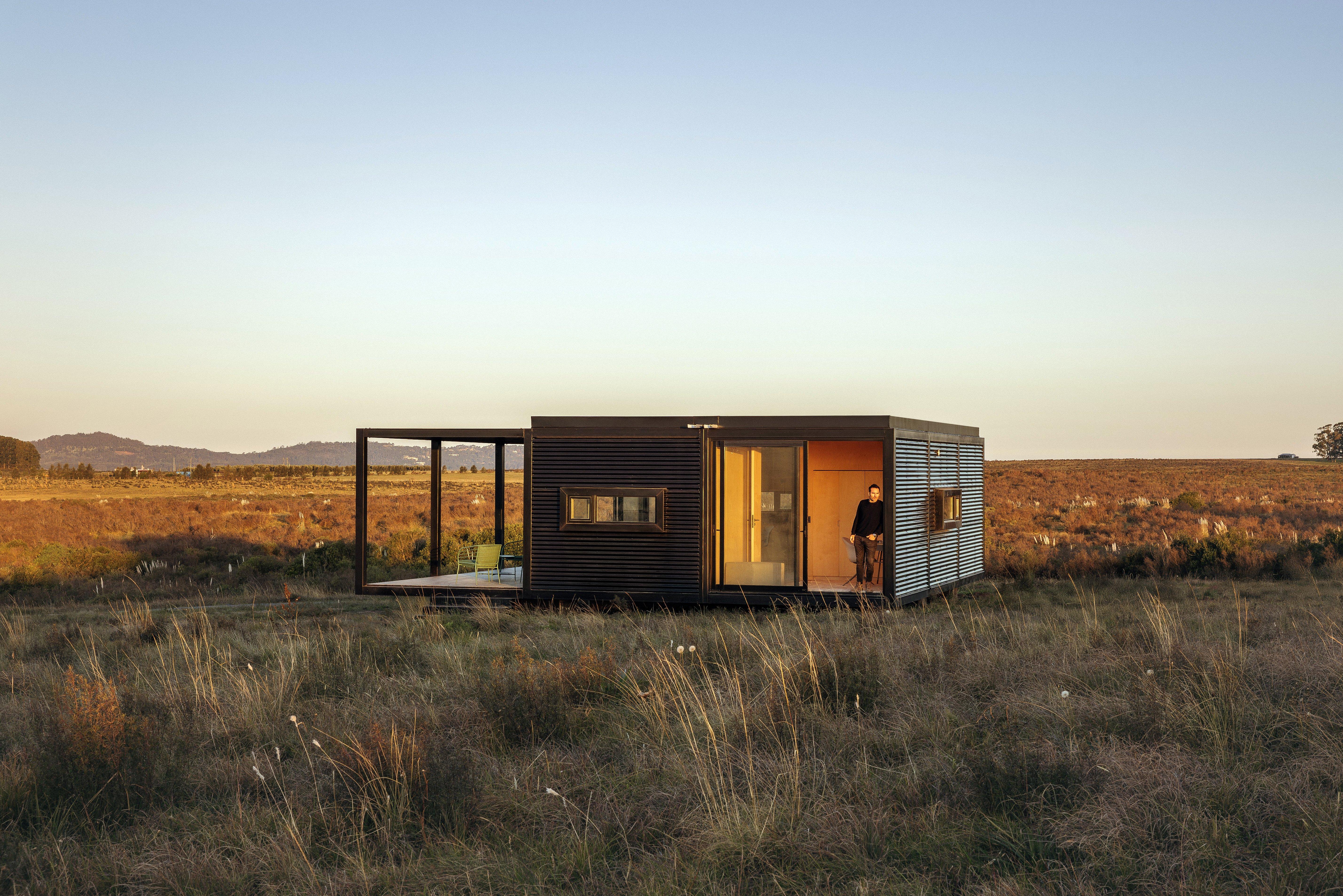 現代化小屋位於草原上，一人站在門口欣賞景色。