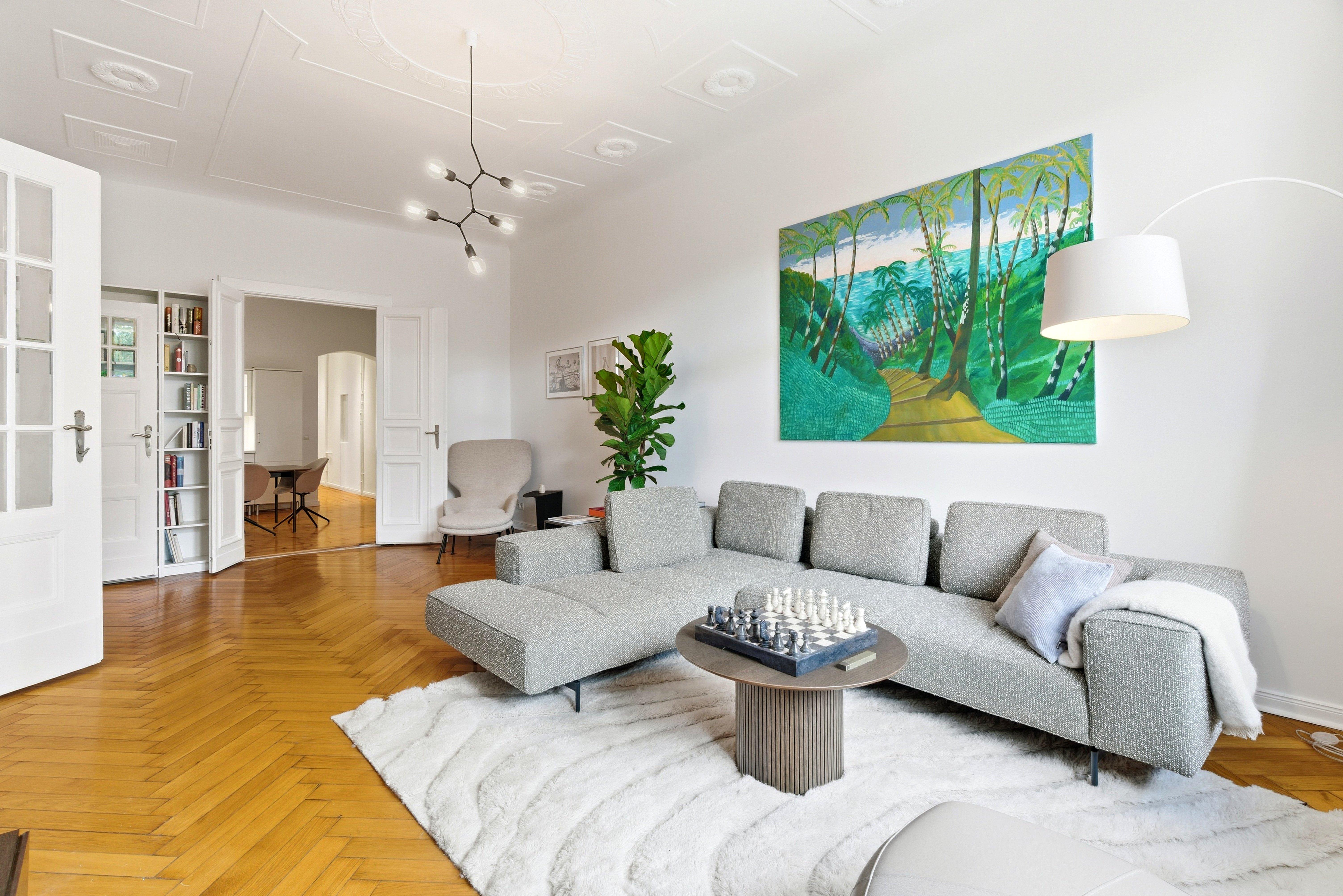 Salon moderne avec canapé gris, table basse ronde, échiquier. Tableau vibrant au mur.
