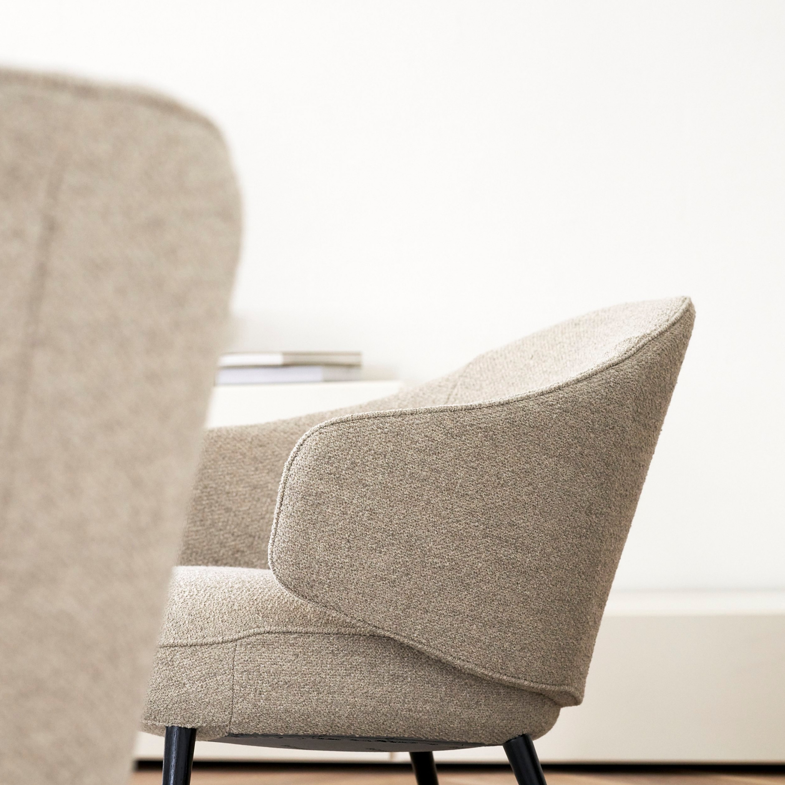 Side view of two textured fabric chairs with black legs in a light interior.