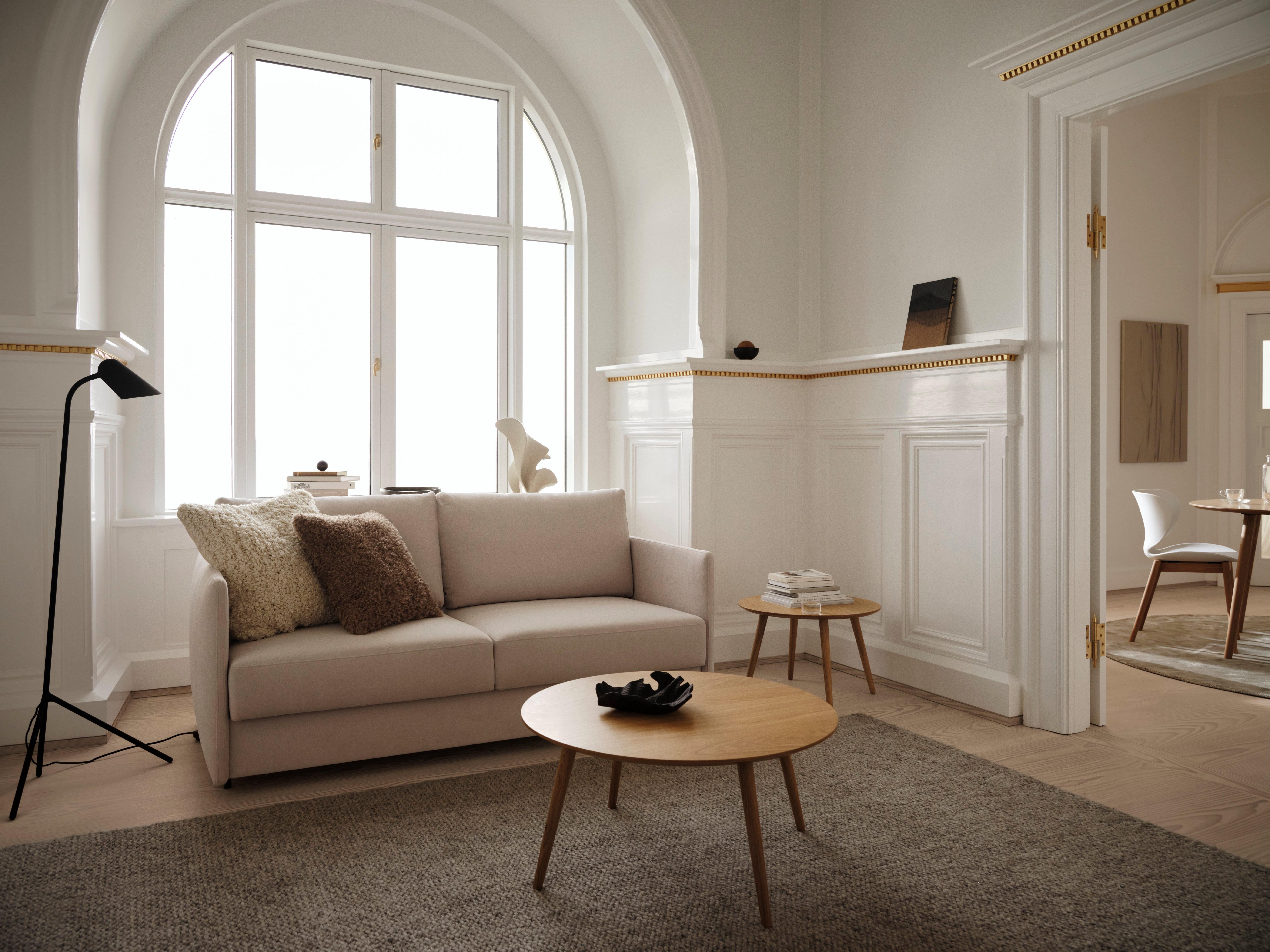 Elegant living room with beige sofa, round wooden tables, and large arched window.