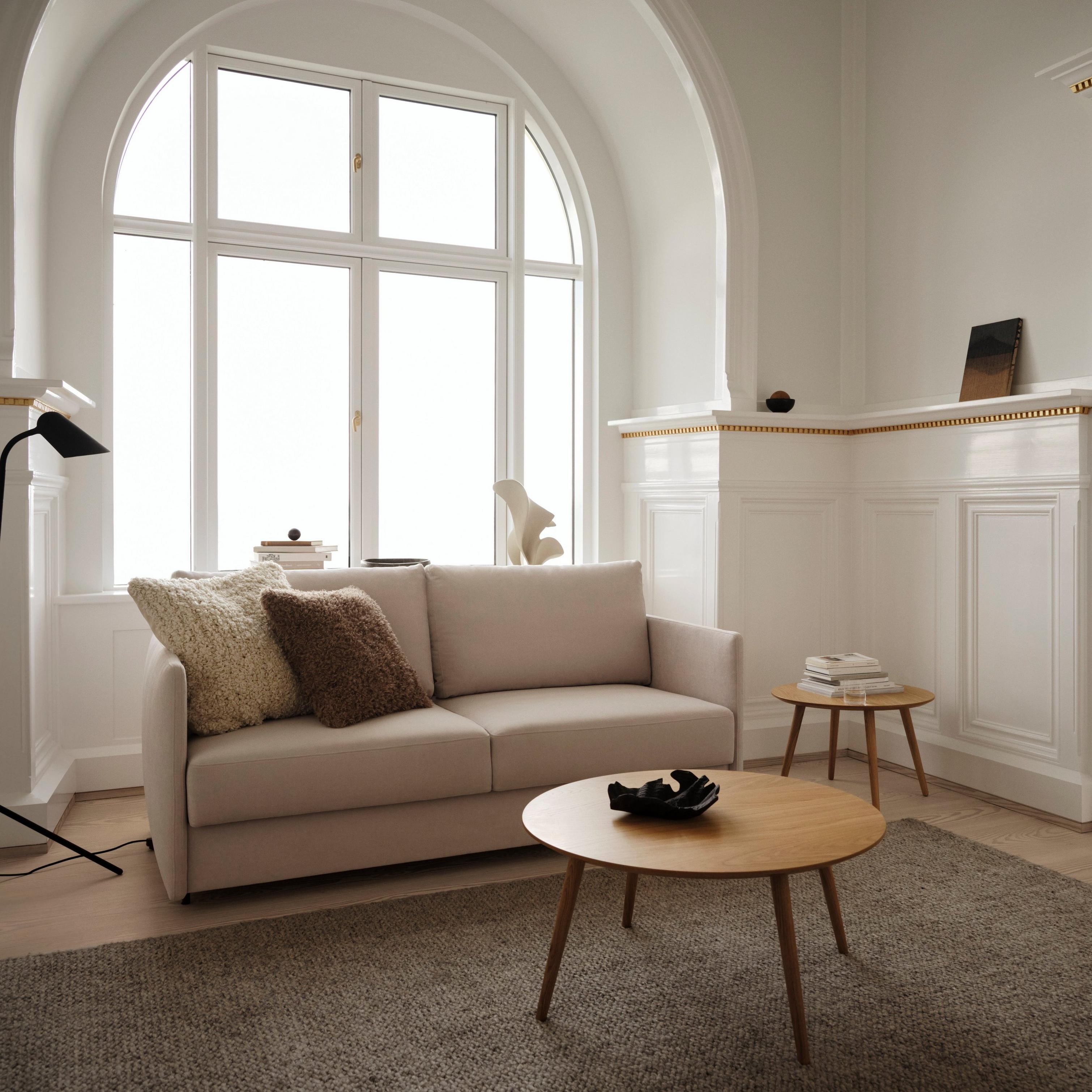 Elegant living room with beige sofa, round wooden tables, and large arched window.