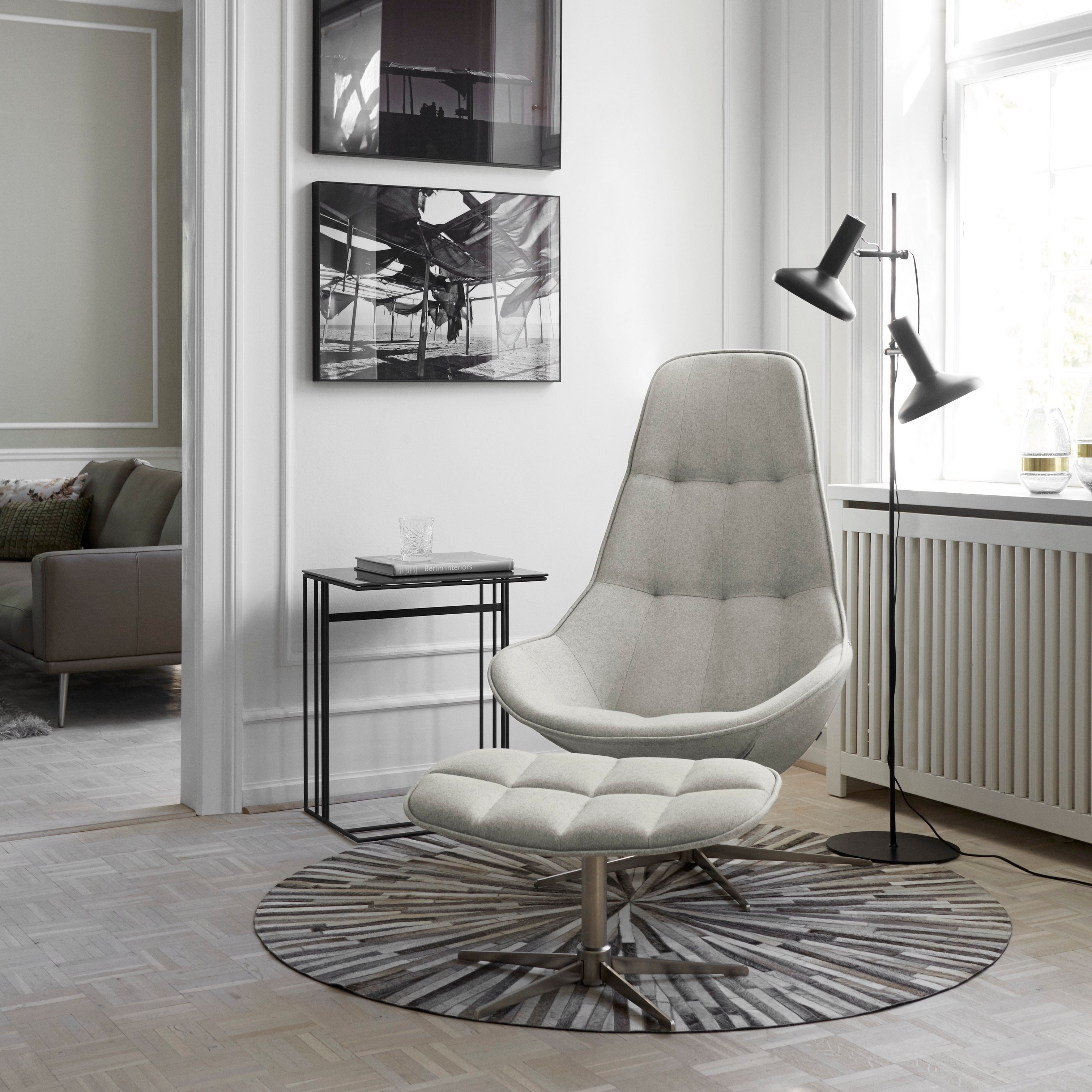 Interior elegante com cadeira de encosto alto, mesa lateral, candeeiro de chão e arte de parede monocromática.