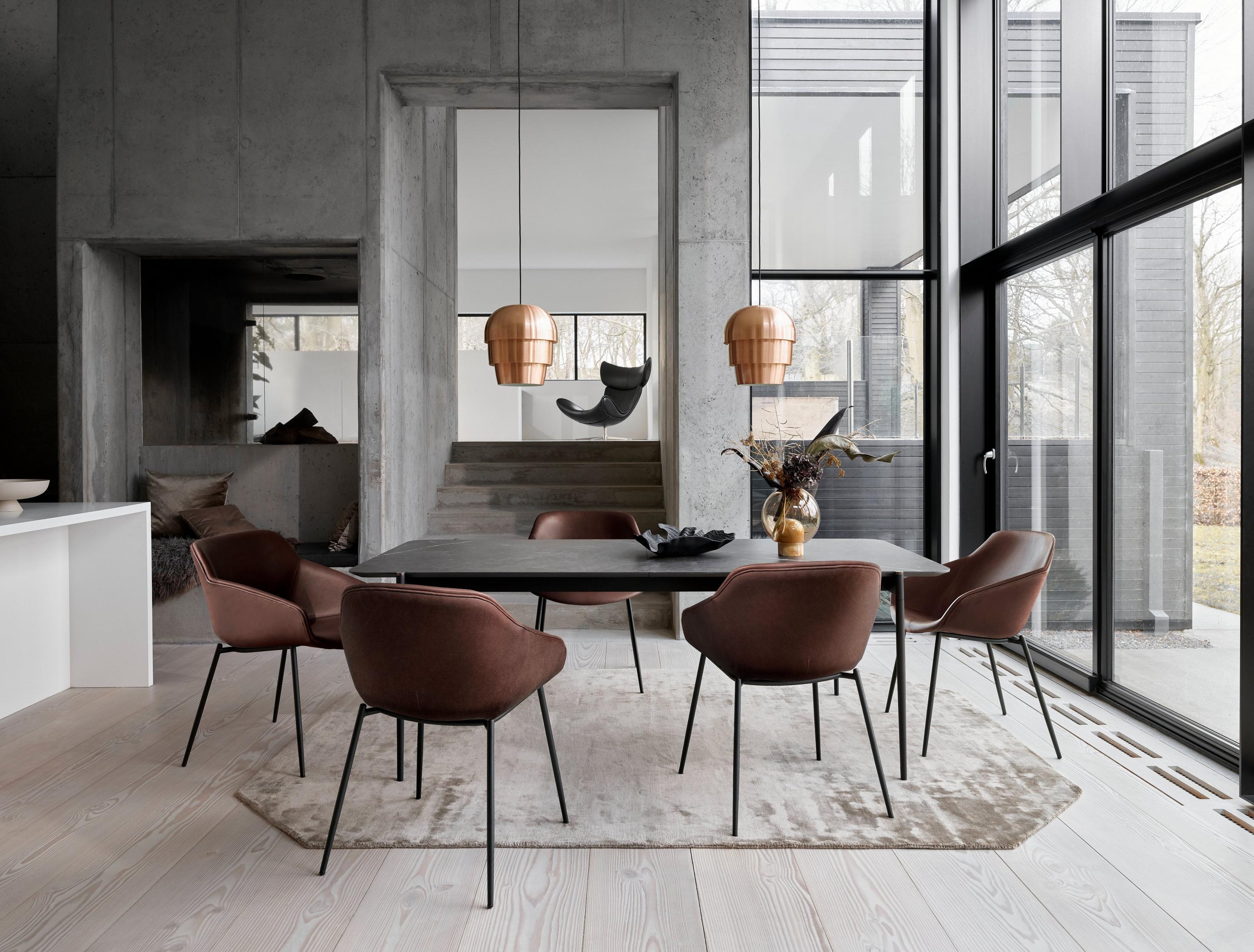 Industrial dining space with brown chairs, black table, copper lamps, and large windows with a garden view.