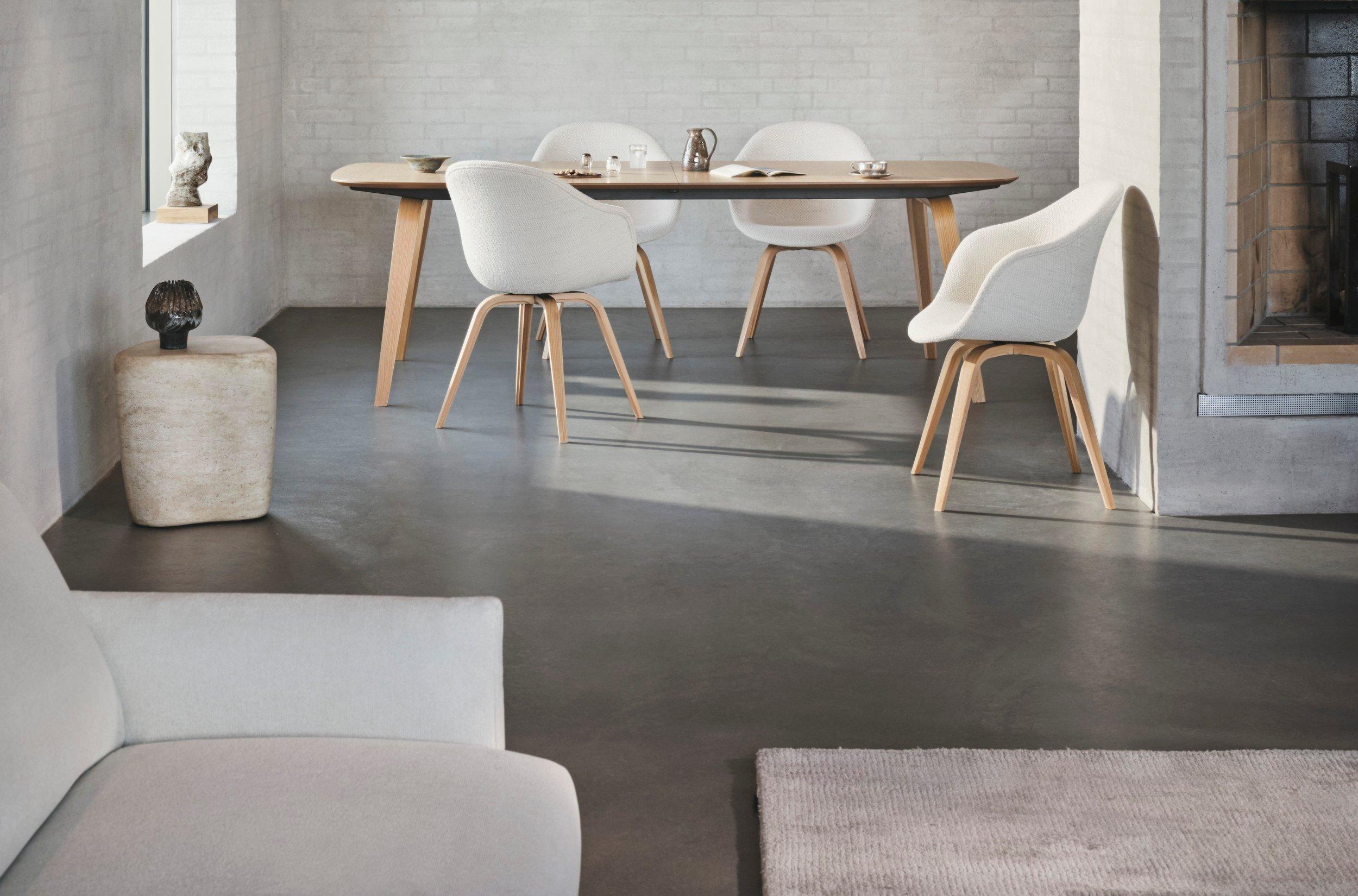 Scandinavian-style dining area with oval wood table, white upholstered chairs, and a fireplace set against light brick walls and wood ceiling.