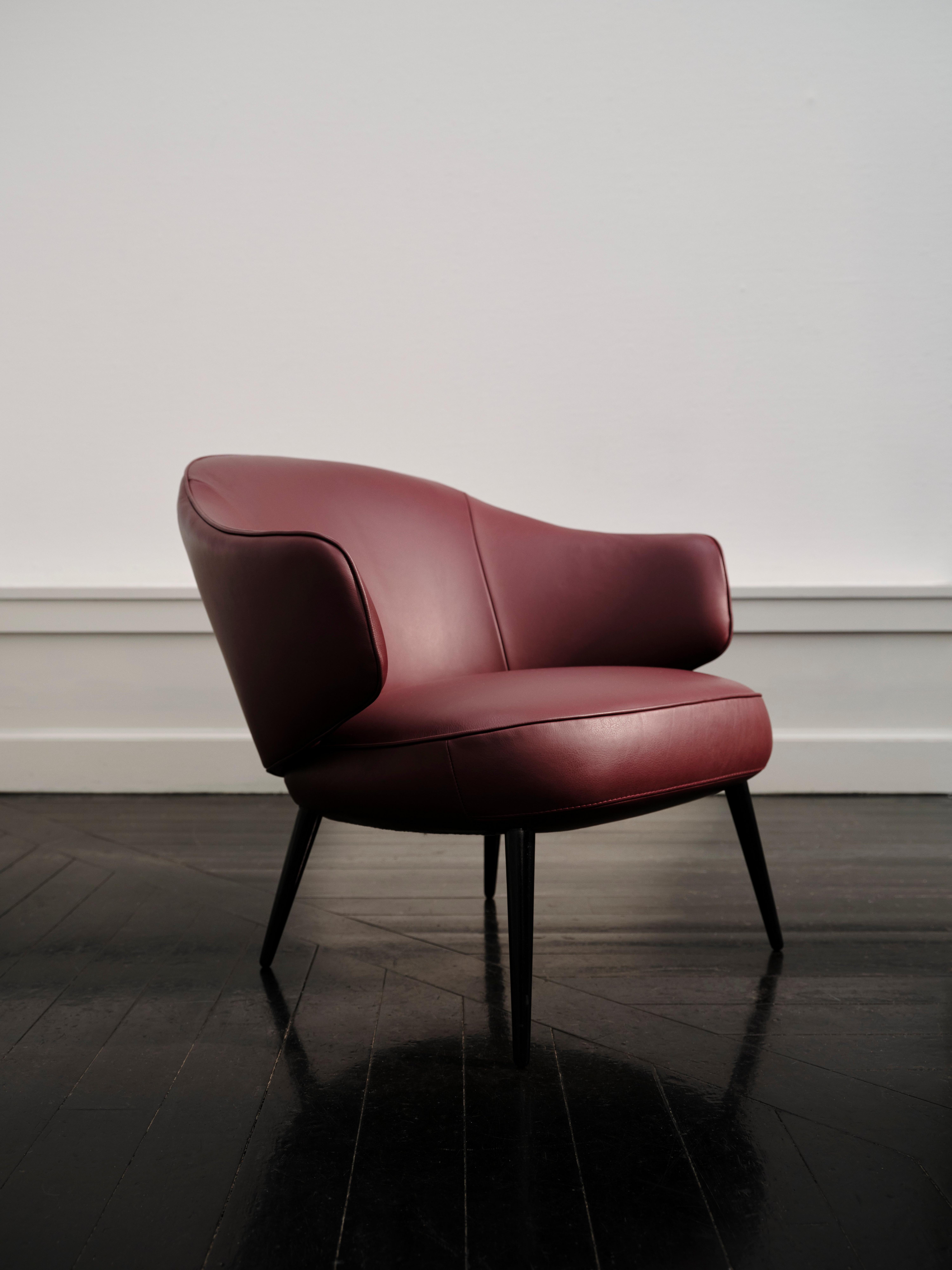 Red upholstered armchair with a curved backrest and black legs on a dark wooden floor.