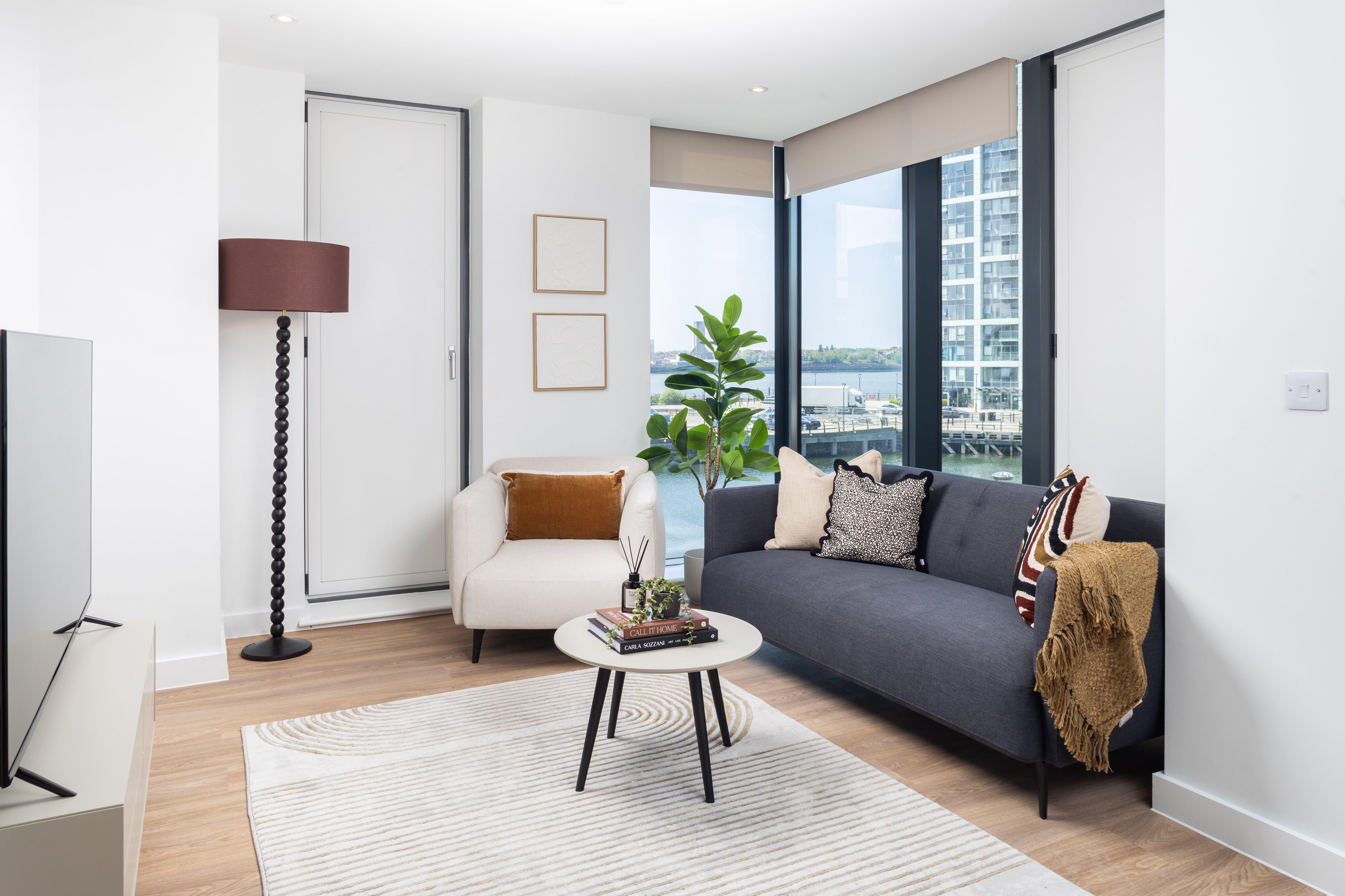 Salón con sofá gris, sillón blanco y mesa redonda con libros y difusor.