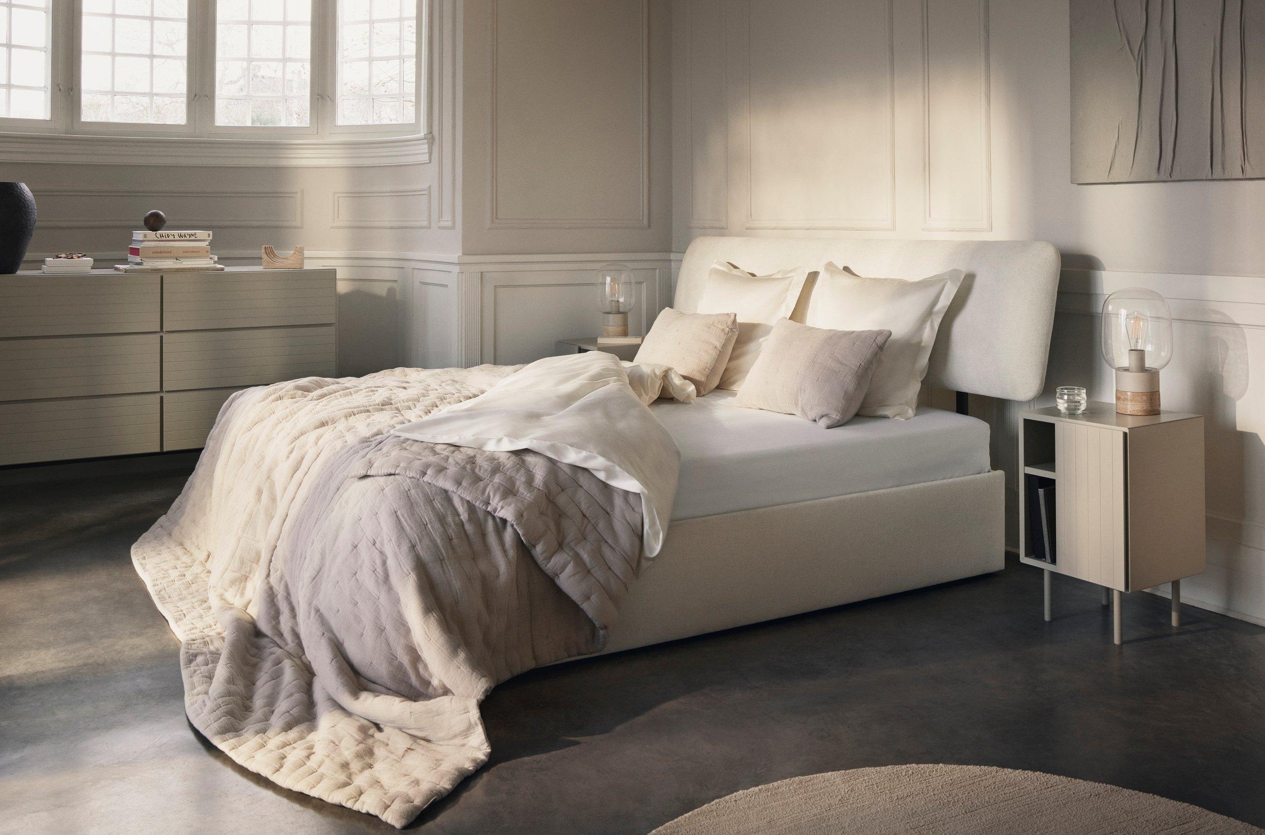 Elegant bedroom with light-upholstered Element bed, neutral bedding, floating nightstand, and large bay window with decorative ceiling.