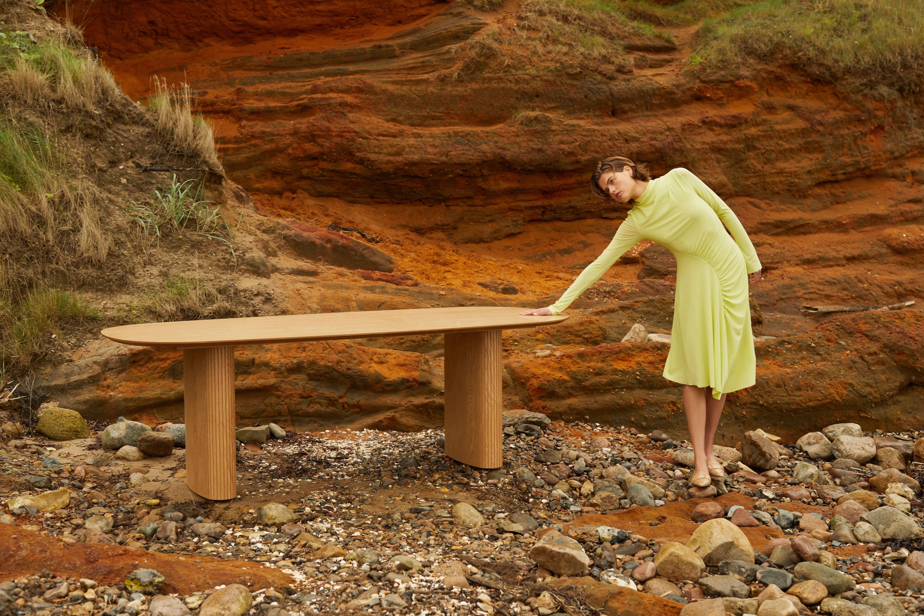 Woman in a yellow dress leaning on a Santiago table against a red clay cliff background.