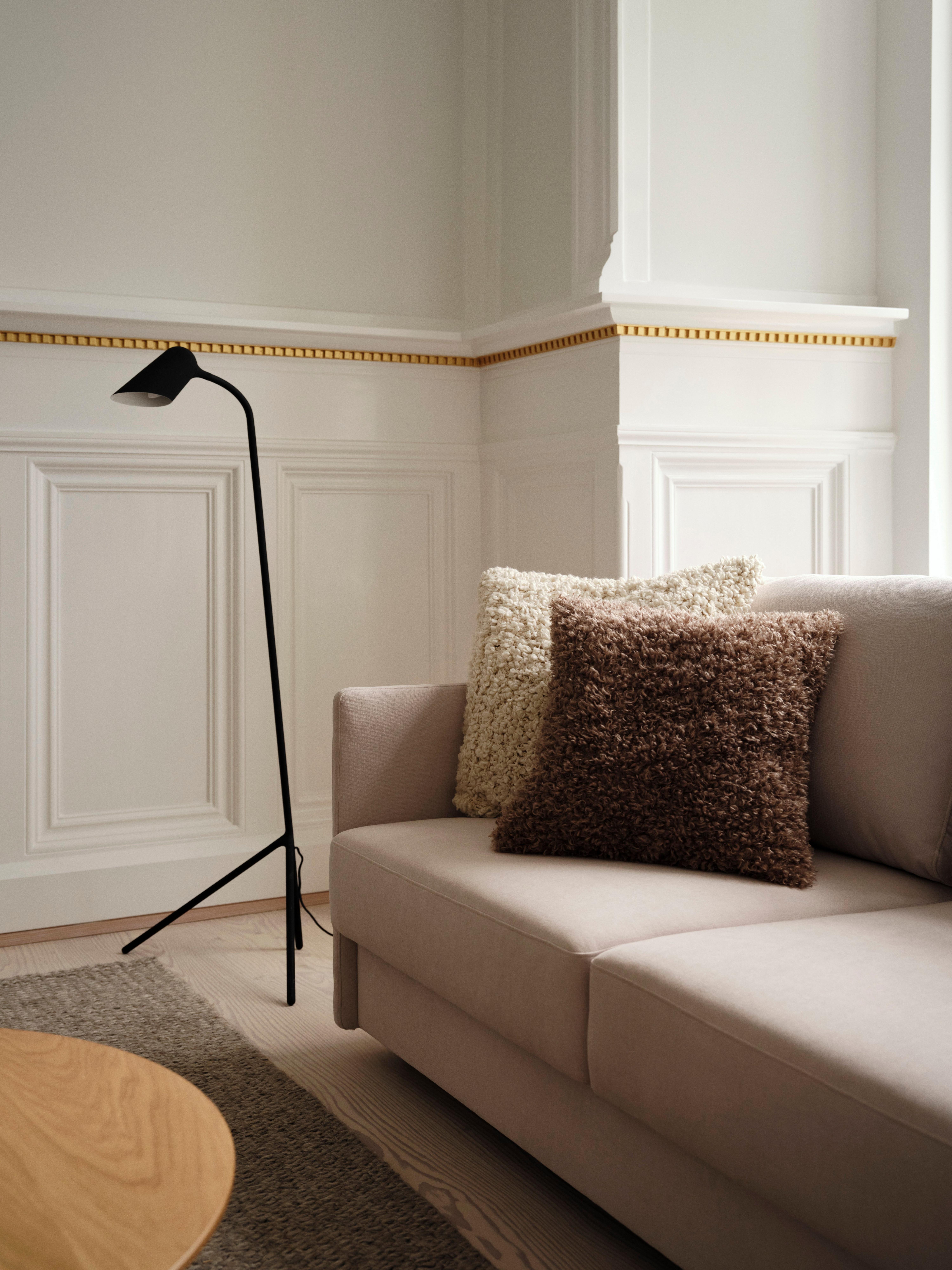 Beige sofa with textured pillows and black floor lamp in elegant room.