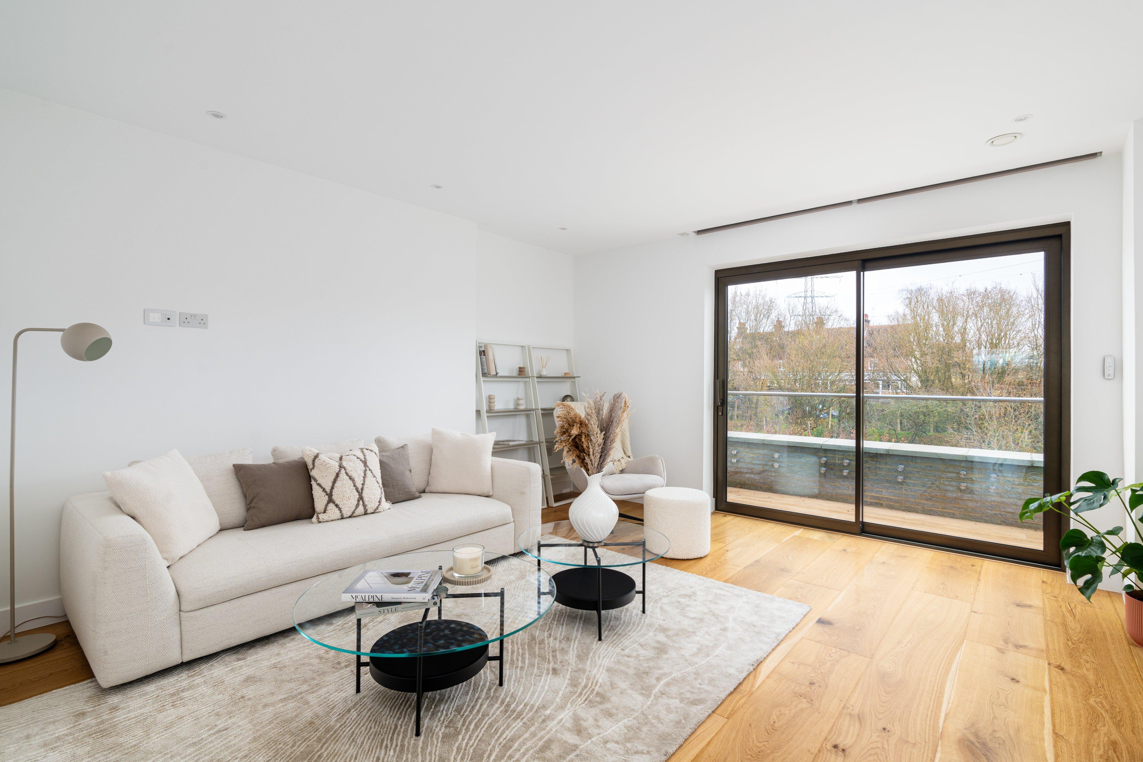 Modern living room with cream sofa, round glass coffee tables and sliding doors to balcony.