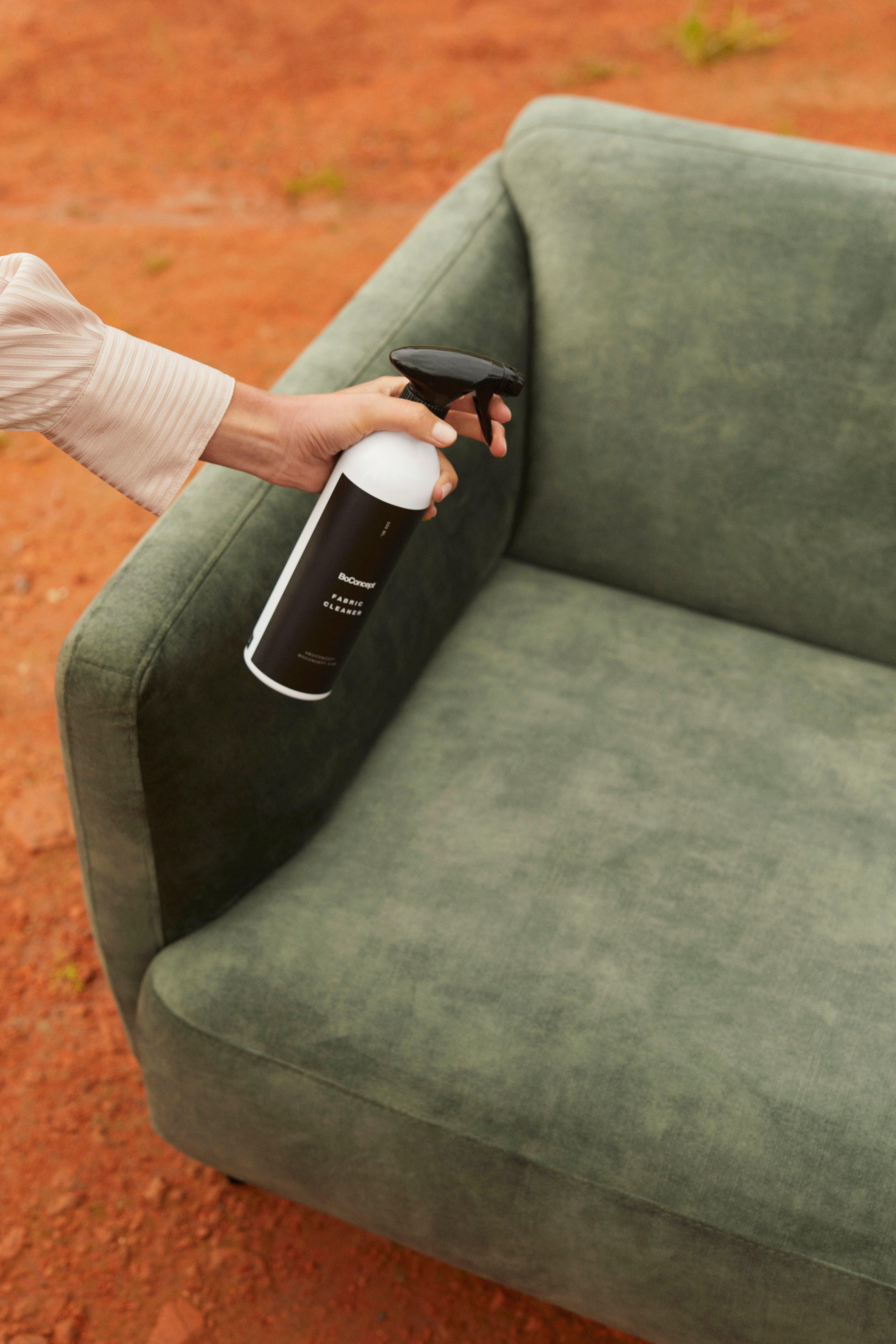 A woman spraying the Modena 2.5 seater sofa in dusty green Ravello fabric with fabric protector.