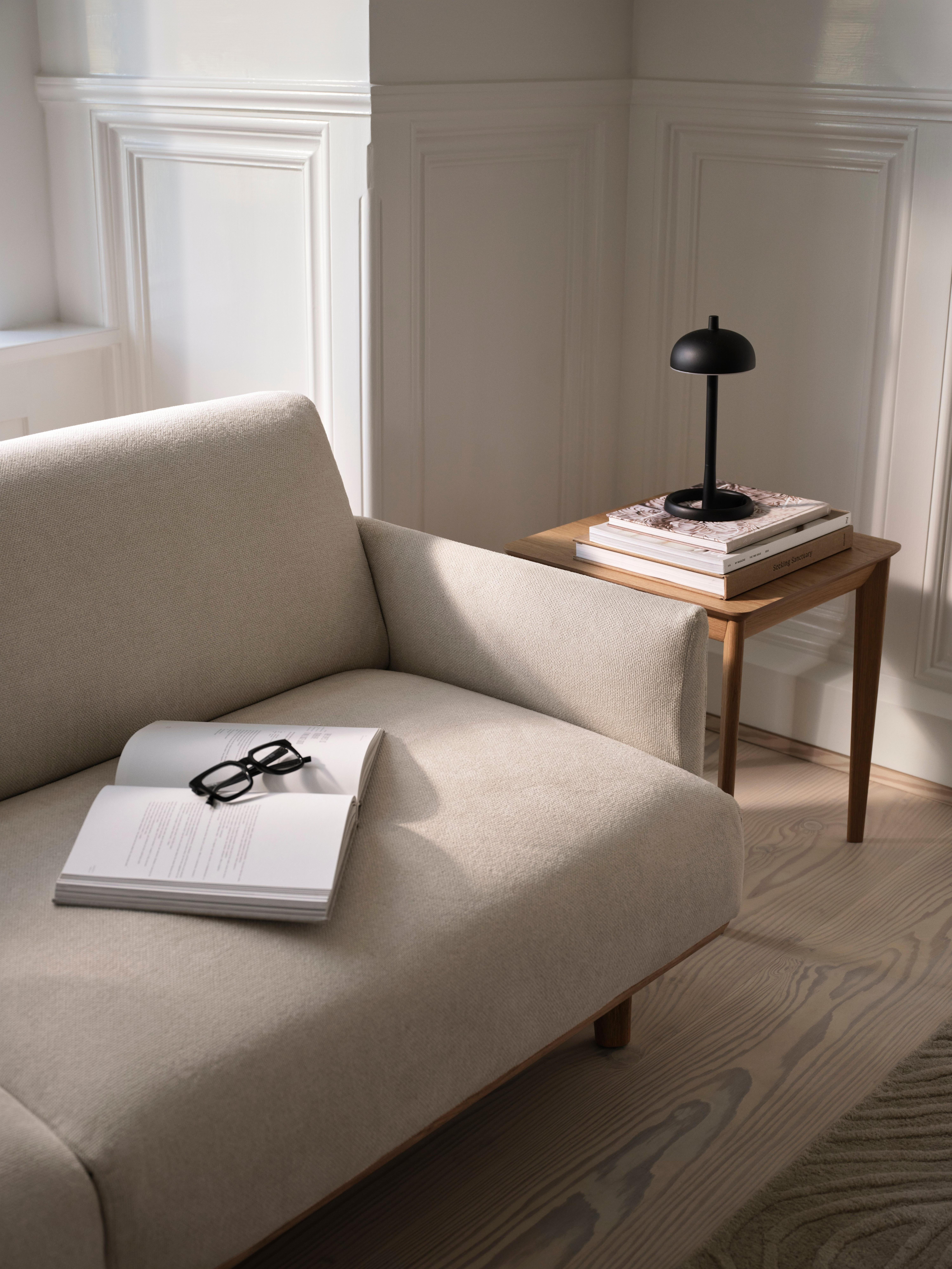 Beige Sofa mit offenem Buch und Brille. Beistelltisch mit schwarzer Lampe und Zeitschriften.