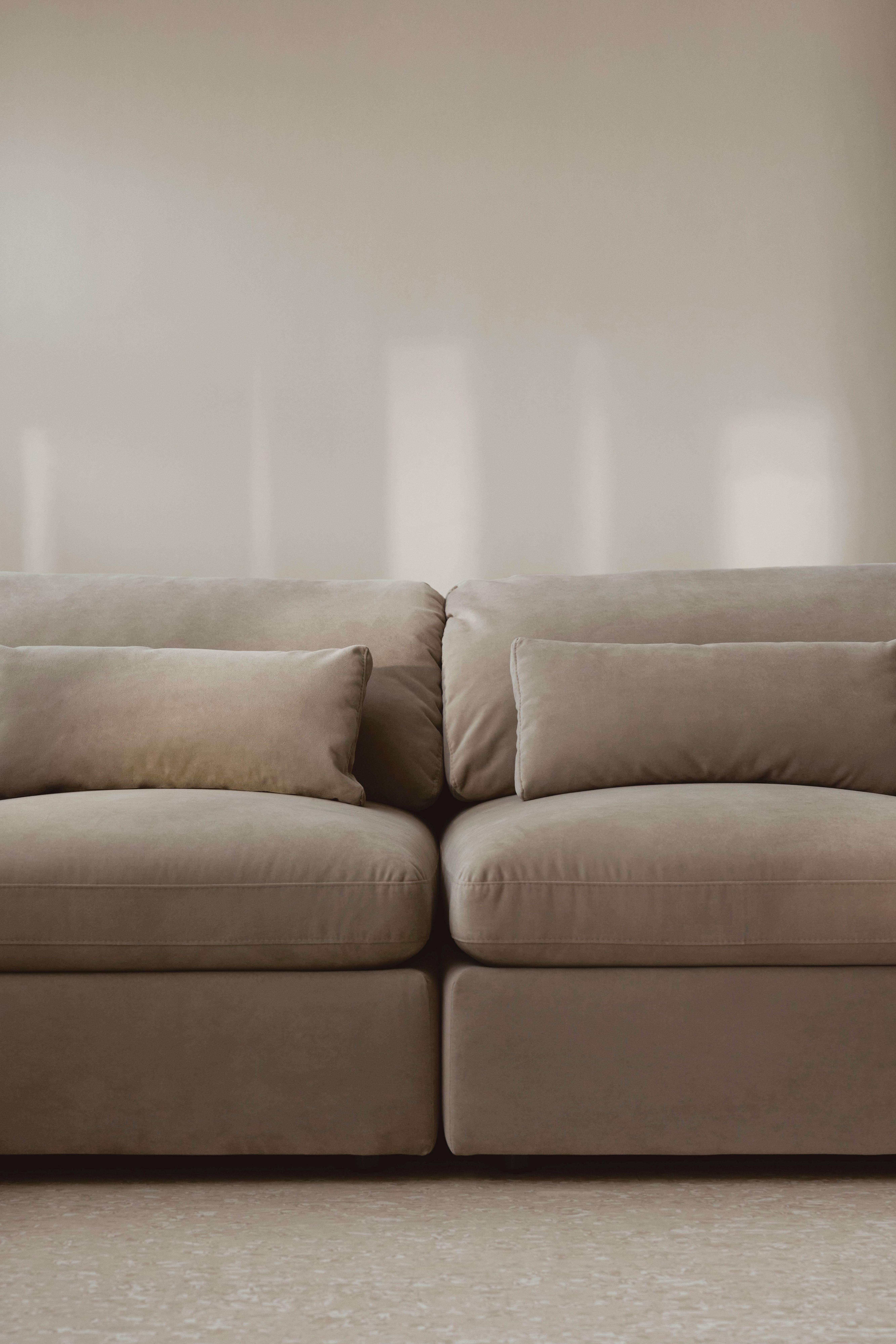 Beige modular sofa with plush cushions and two matching pillows, set against a neutral-toned wall and light flooring.