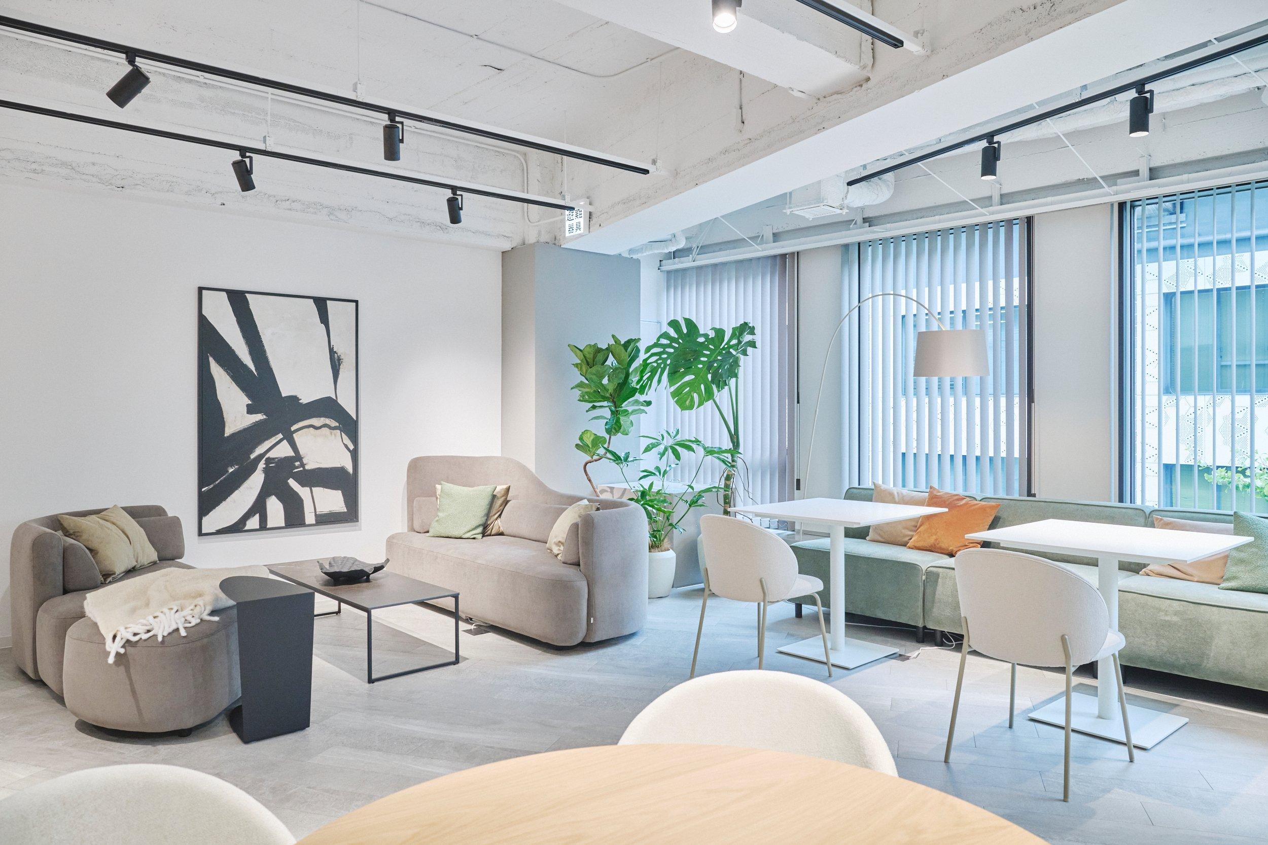 Sala moderna con sofás grises, mesas blancas, y plantas. Arte abstracto en la pared.