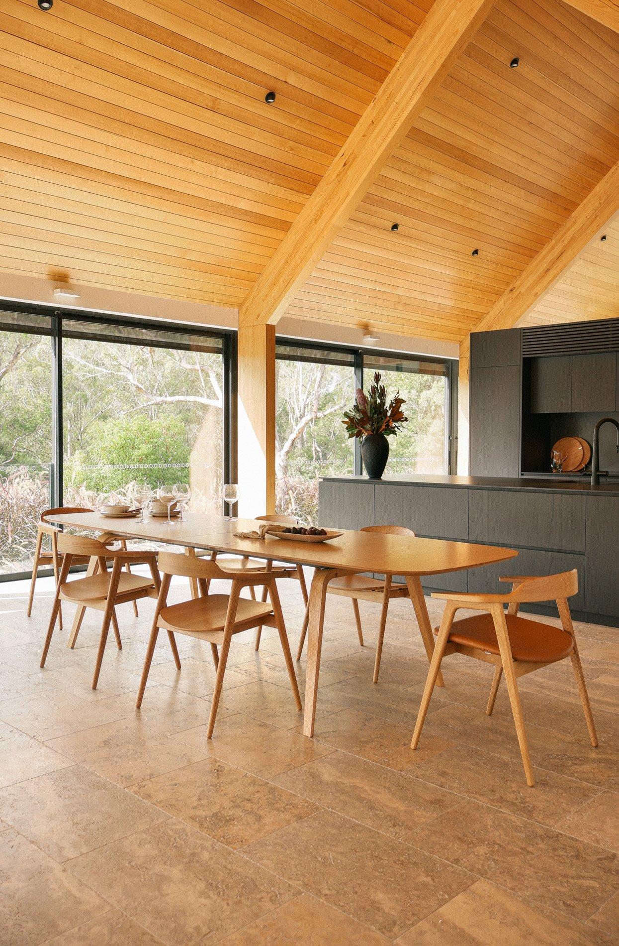 Wooden dining table with four matching chairs, set with glassware in a modern kitchen.